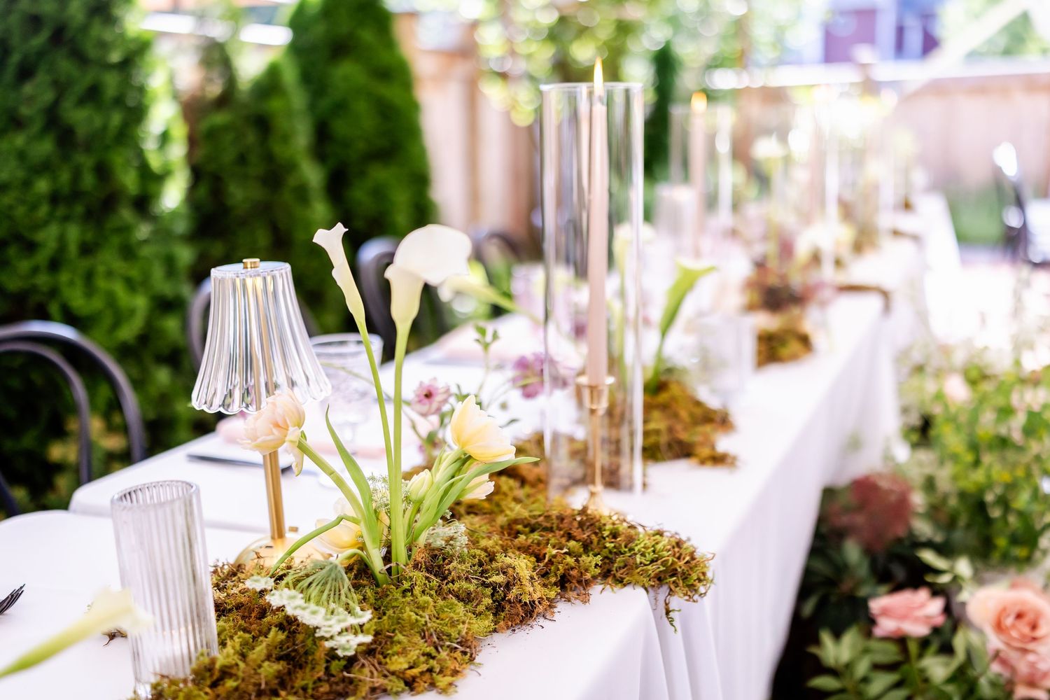 A rustic garden-themed wedding table setting with moss, white candles, and delicate floral arrangements.