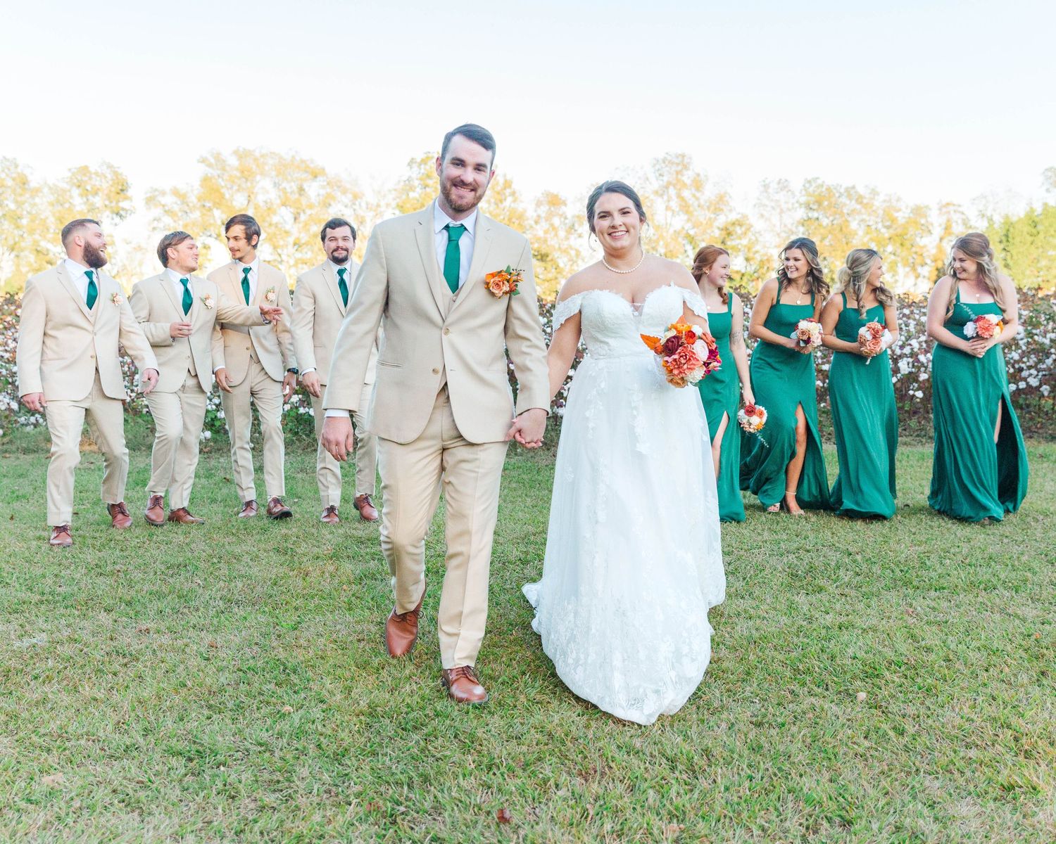 Wedding party in teal dresses and tan suits poses on grassy hill during outdoor celebration.