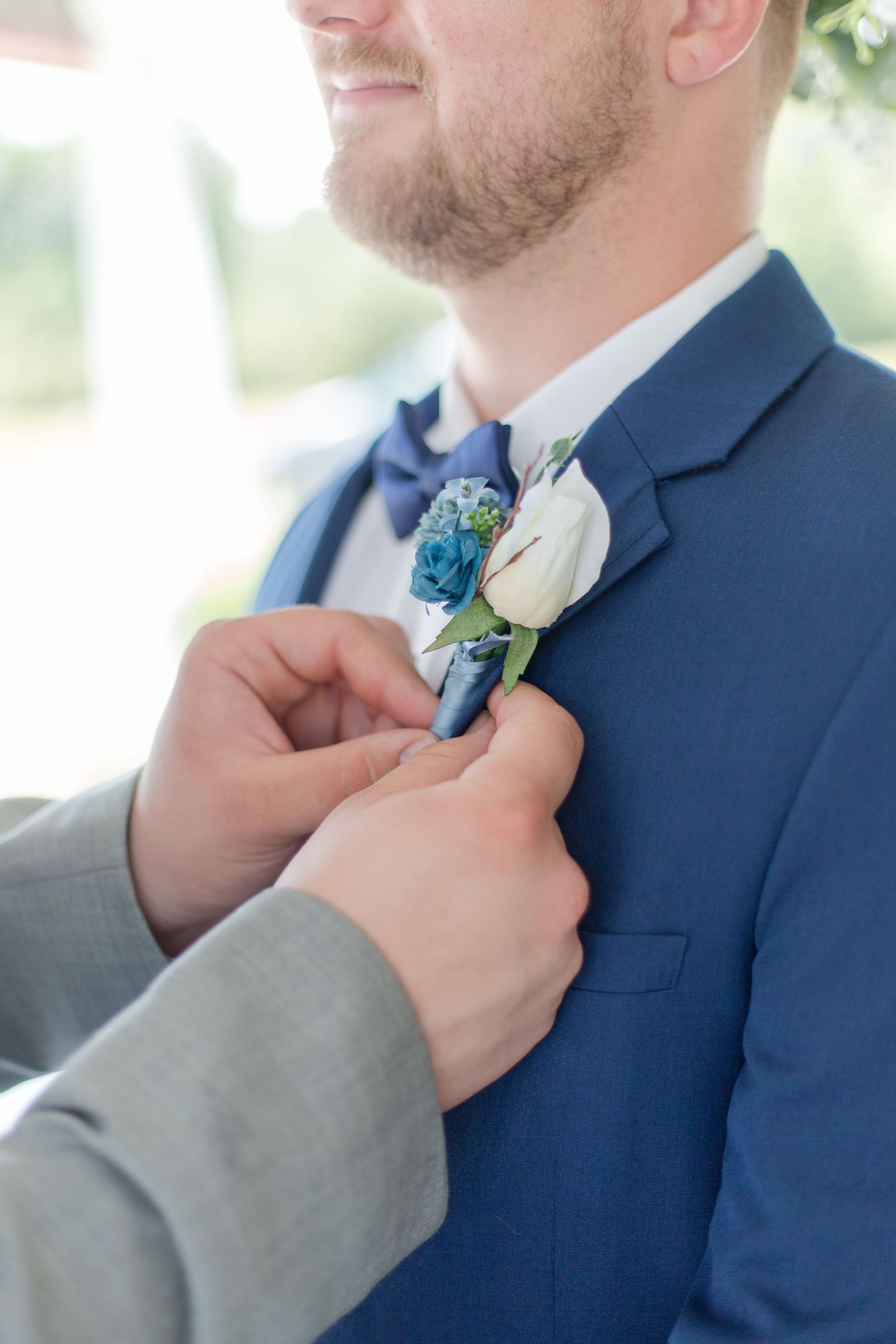Groomsman adjusting blue boutonniere on navy suit jacket.