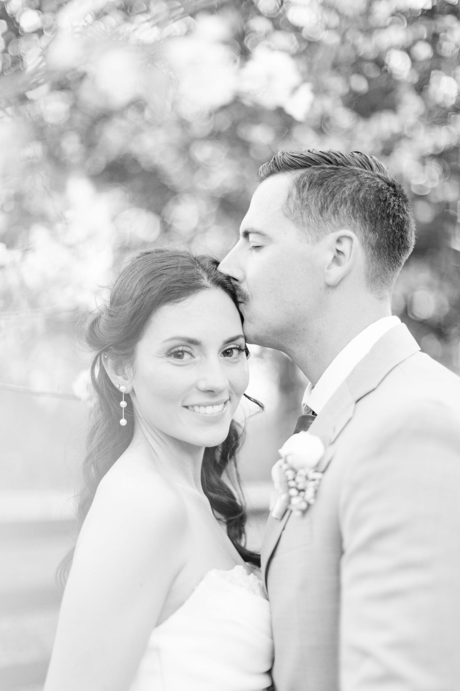 Romantic black and white portrait of newlyweds sharing an intimate moment with dreamy bokeh background.