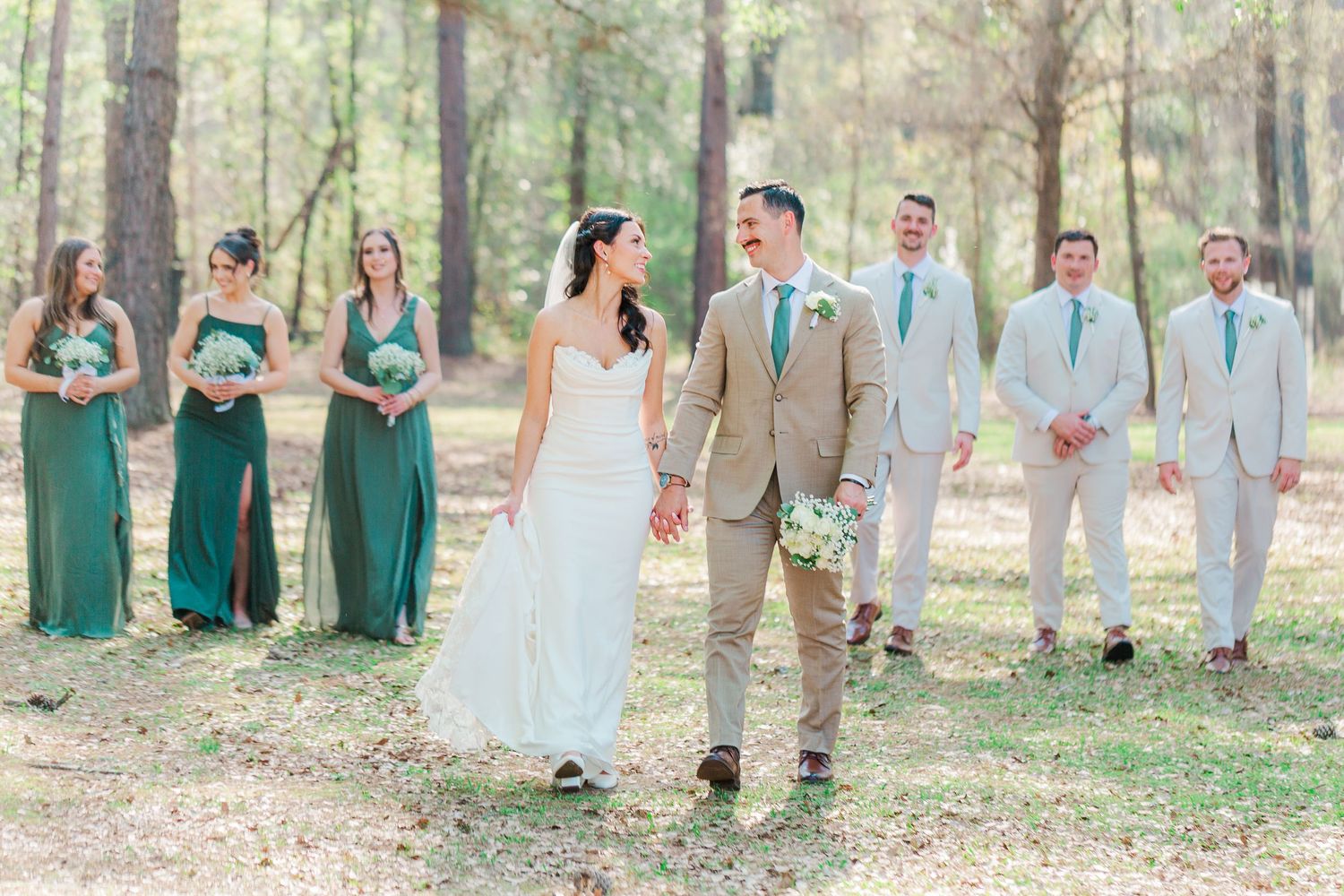 Wedding party in forest setting with bridesmaids in emerald green dresses and groomsmen in light suits.