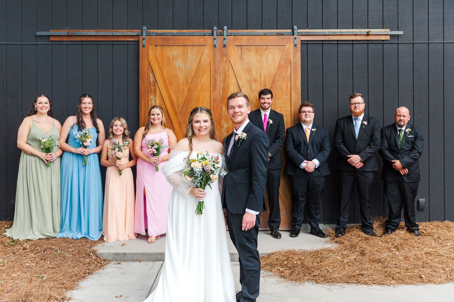 Wedding party posed in front of black barn with sliding door.