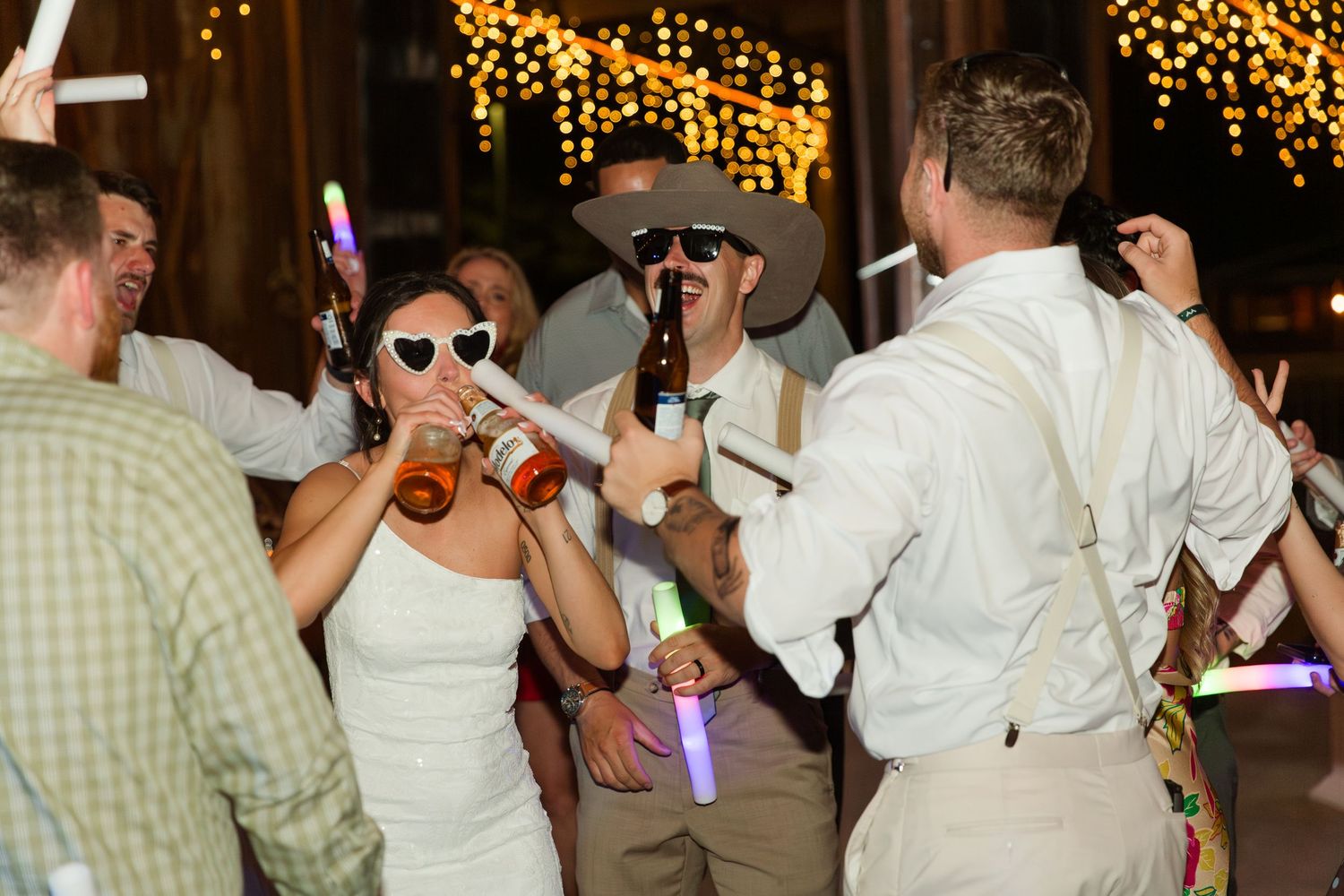 Wedding guests dance and celebrate on a festively lit dance floor at an indoor reception venue.