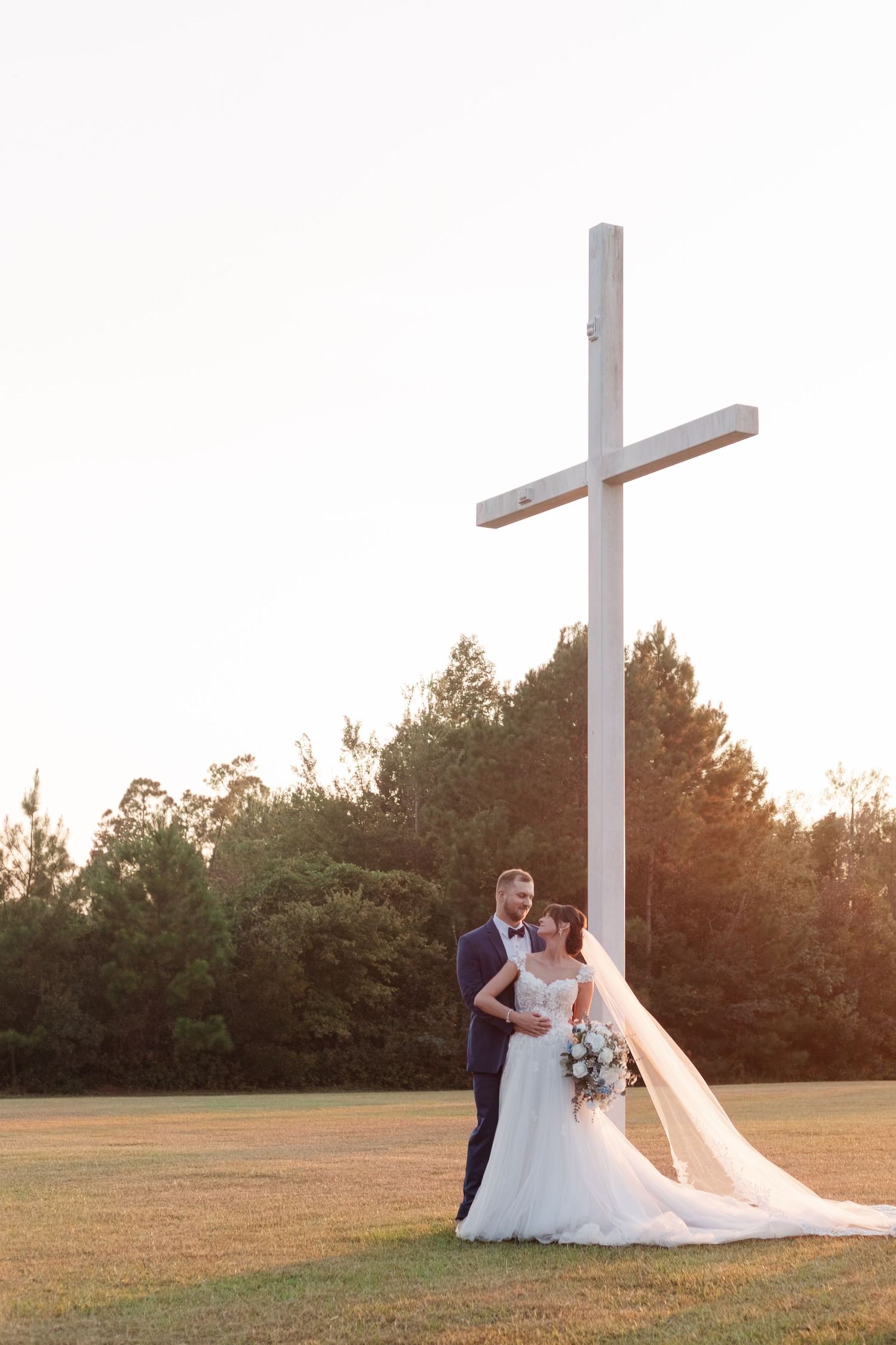 Wedding couple poses near white crosses in a field during golden hour sunset.