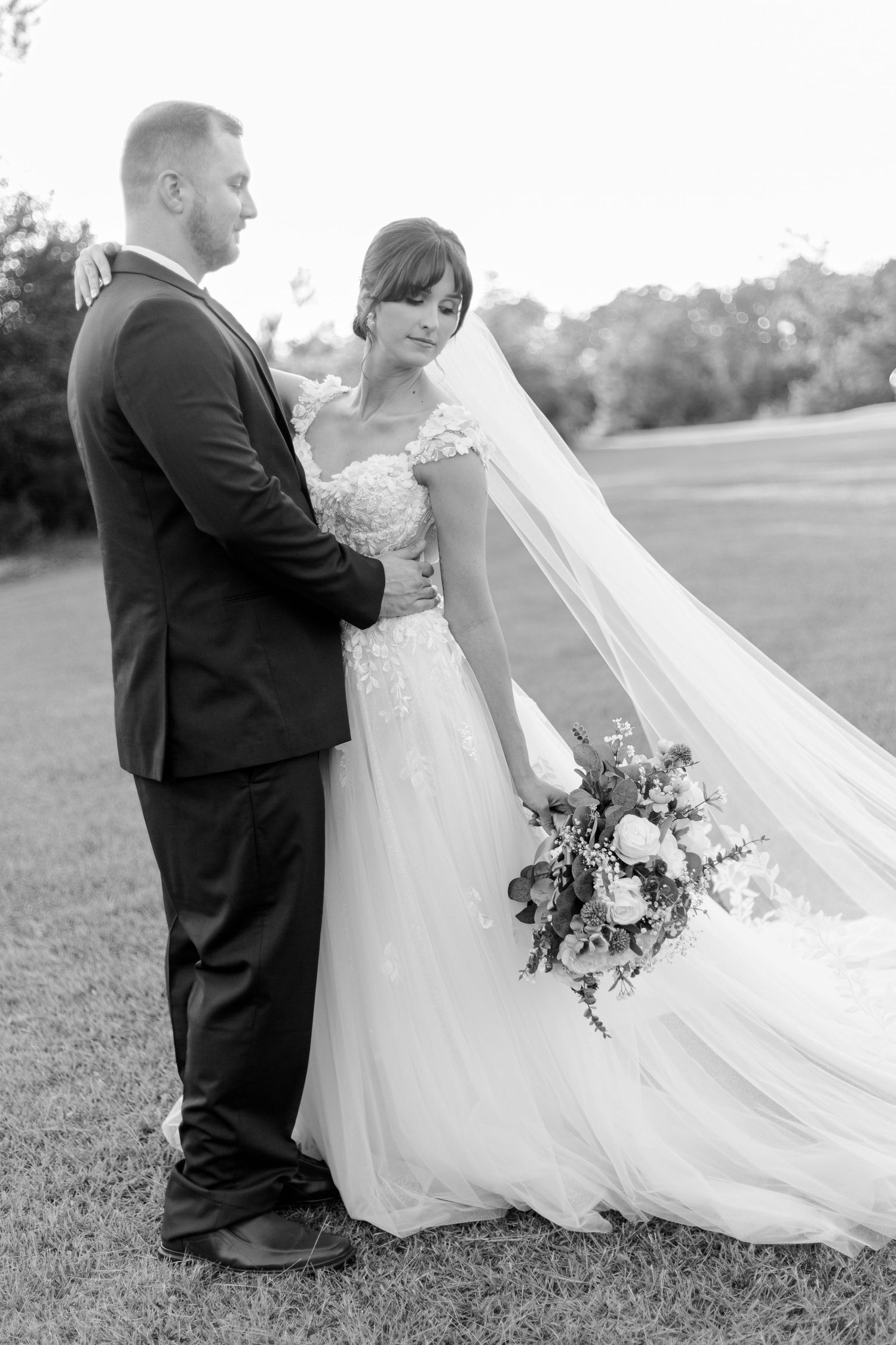 A wedding couple embraces in a series of romantic black and white photos in an outdoor field.