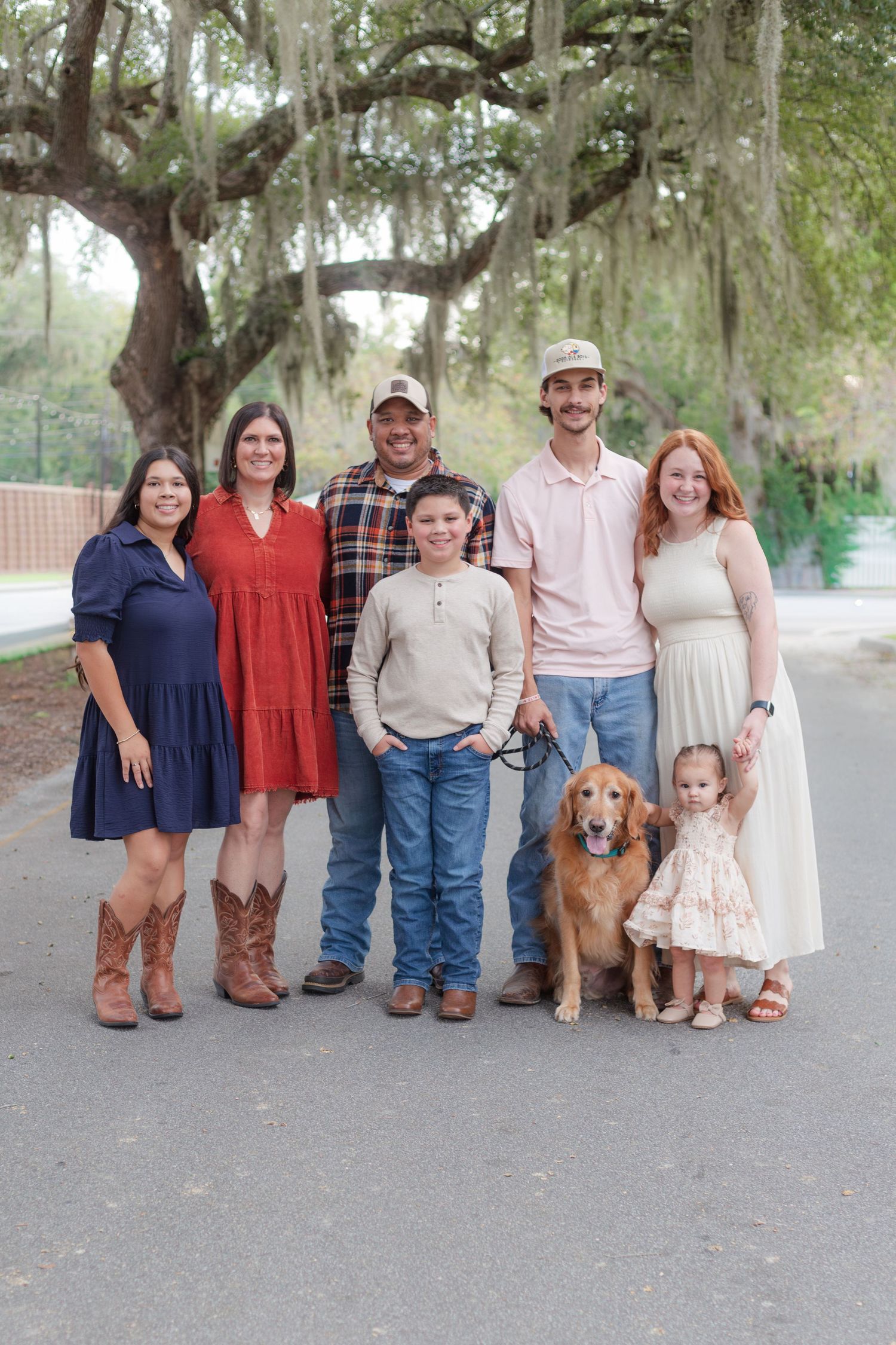 Family group photo with golden retriever dog under moss-draped oak trees.
