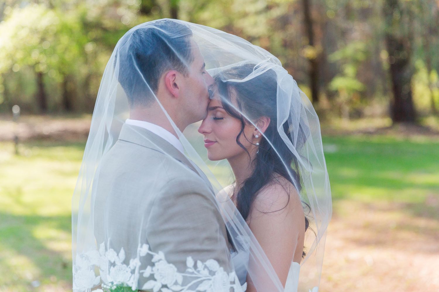Romantic moment captured under bridal veil during spring outdoor wedding portraits.