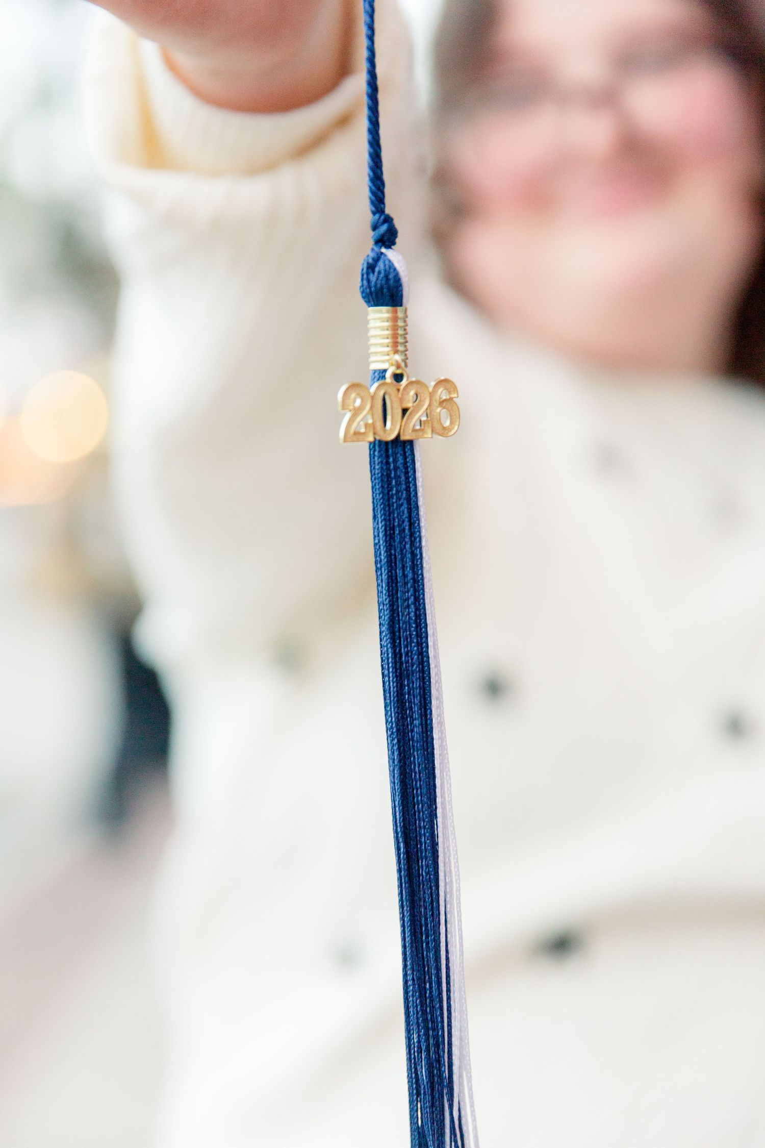 Blue graduation tassel with gold 2023 charm hanging against blurred background.