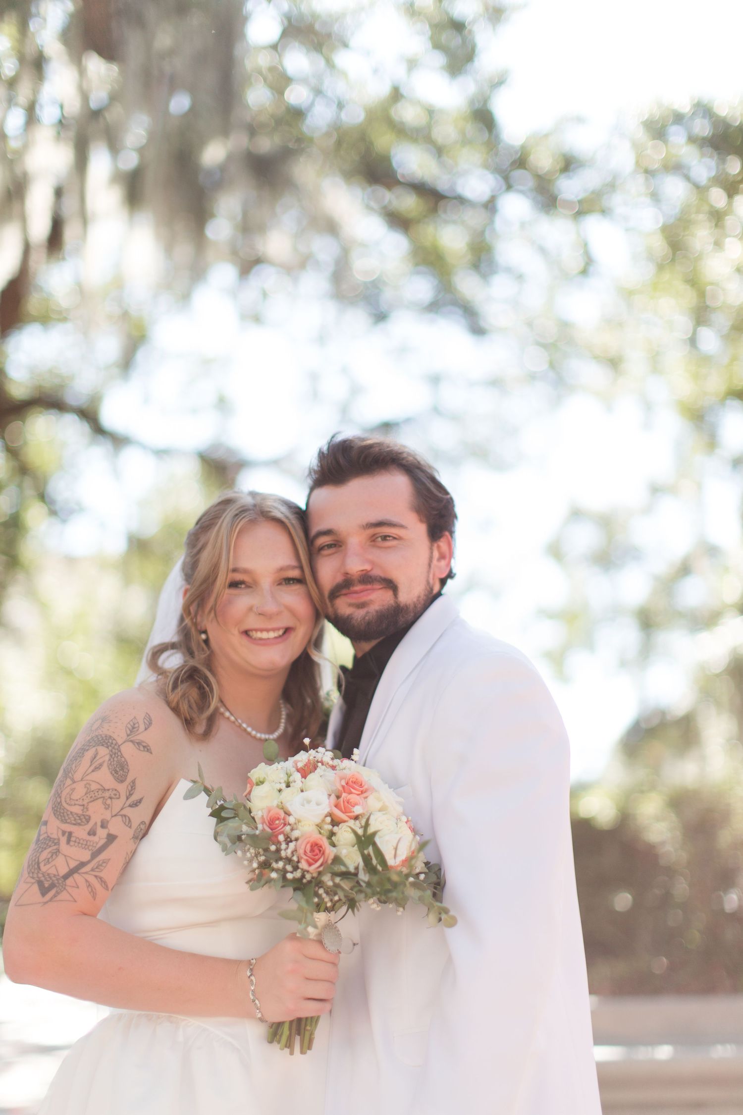 Wedding couple embraces in sunny outdoor setting with trees in background.
