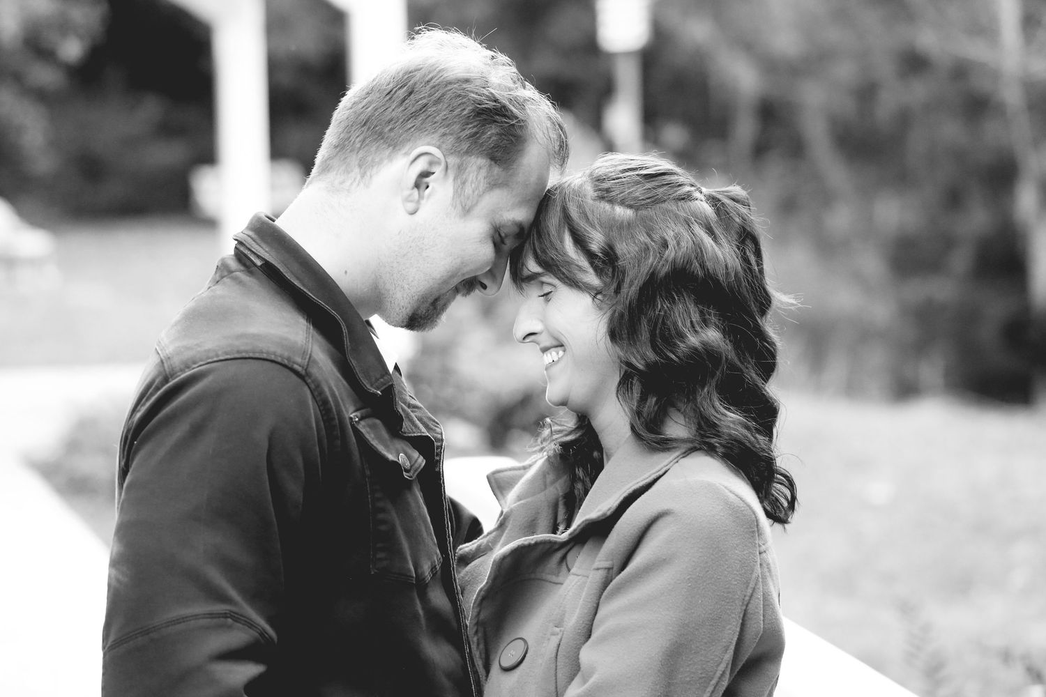 Black and white photo of couple sharing intimate moment under garden structure.