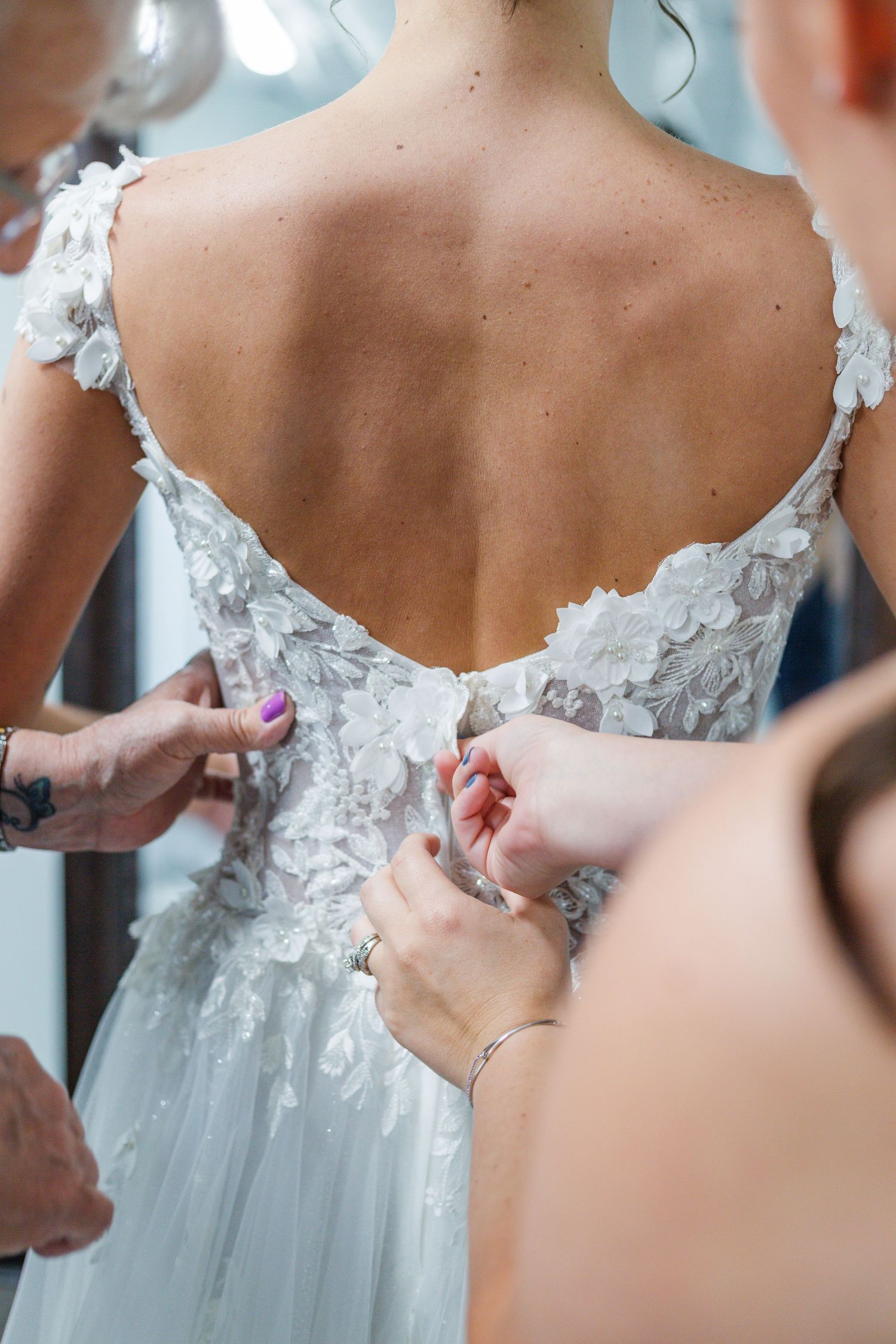 Close-up of intricate lace details being fastened on back of wedding gown.