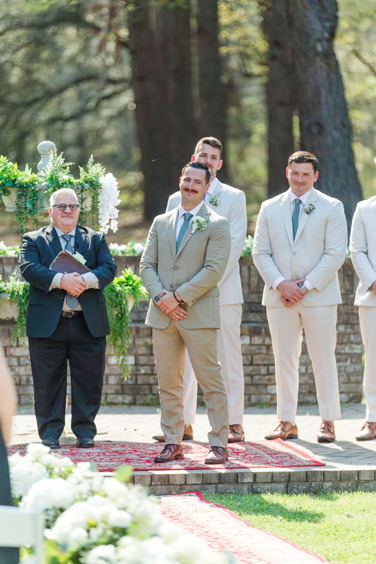 Wedding party stands at decorated outdoor altar with floral arrangements and vintage brick details.