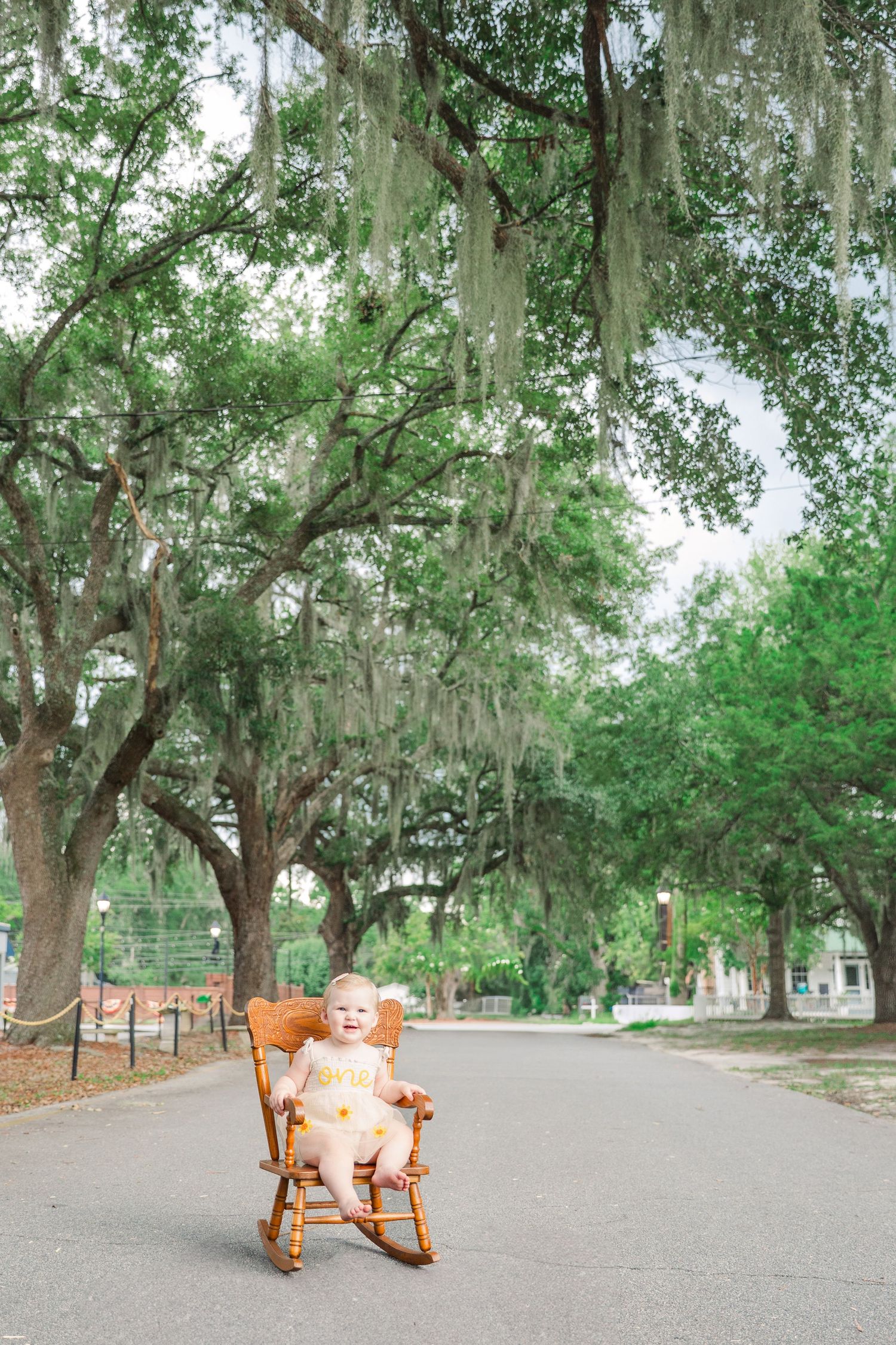 A rustic wooden rocking chair sits on a path under Spanish moss-draped trees.