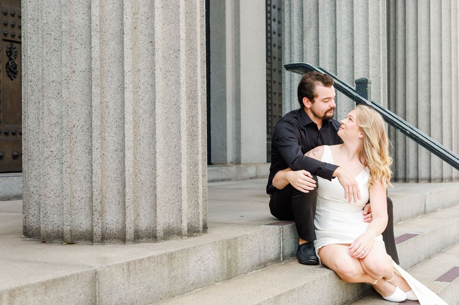 Romantic wedding couple poses against classic stone columns in elegant formal attire.