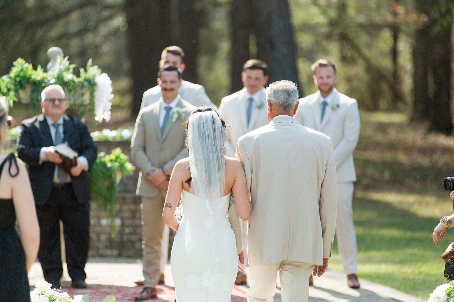Wedding party members in tan and beige formal attire walking together outdoors during a ceremony.