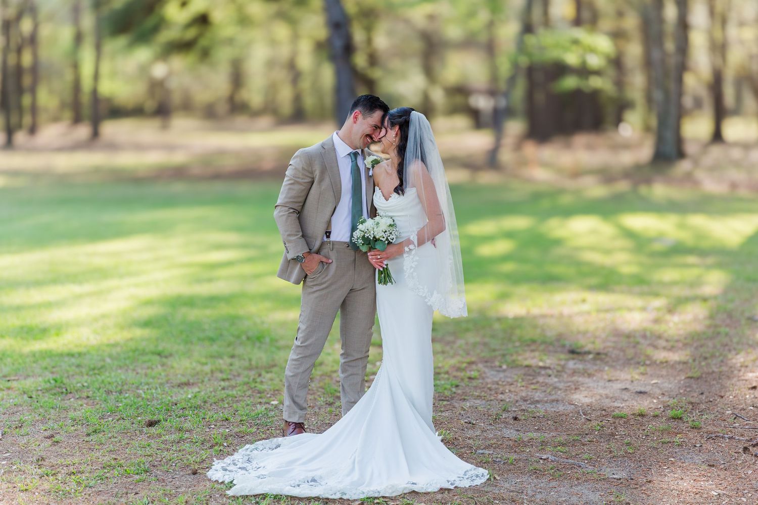 Wedding party poses along tree-lined path with bridesmaids in emerald dresses and groomsmen in grey suits.