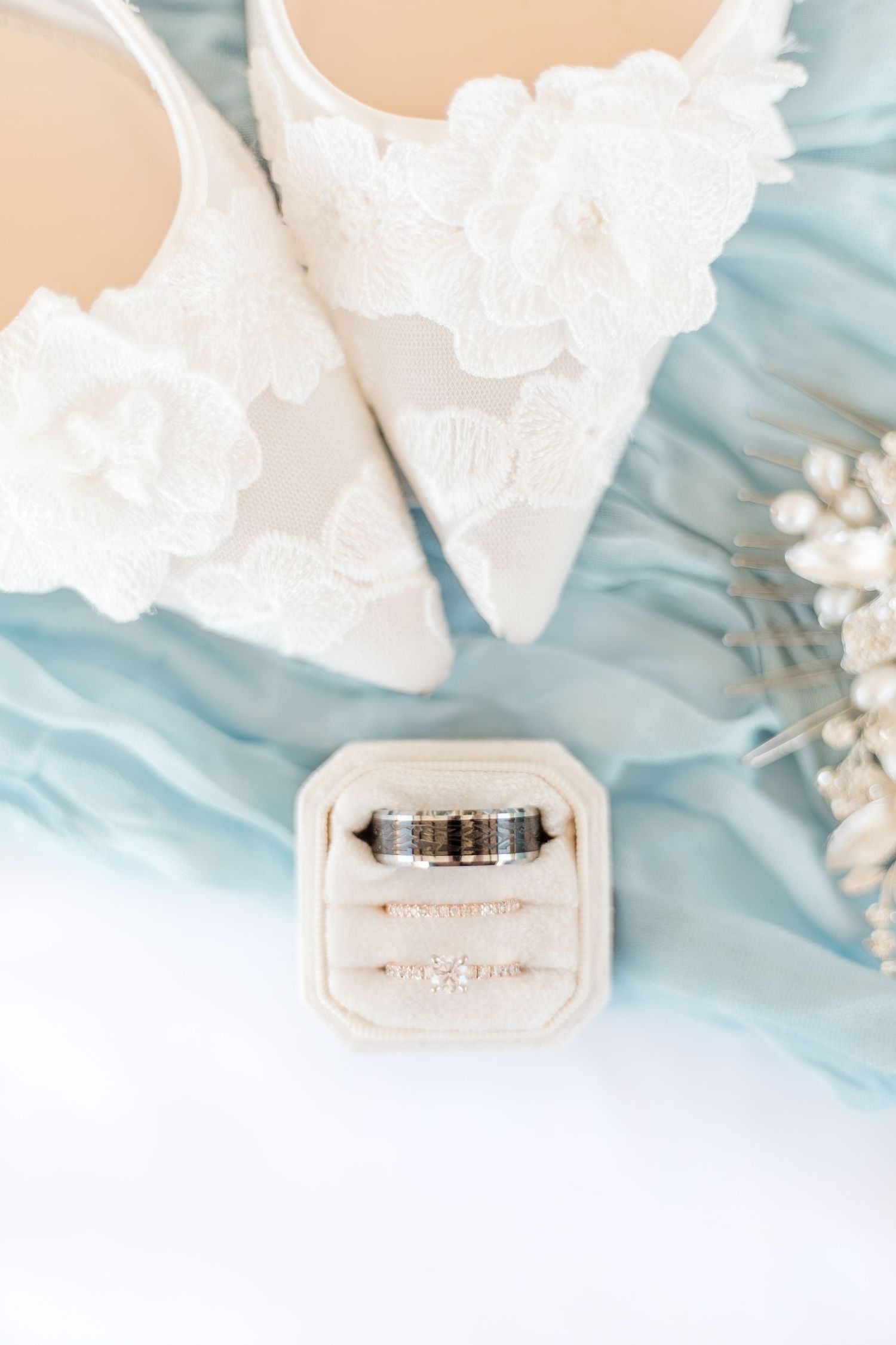 Elegant lace wedding shoes and wedding rings styled on blue fabric.