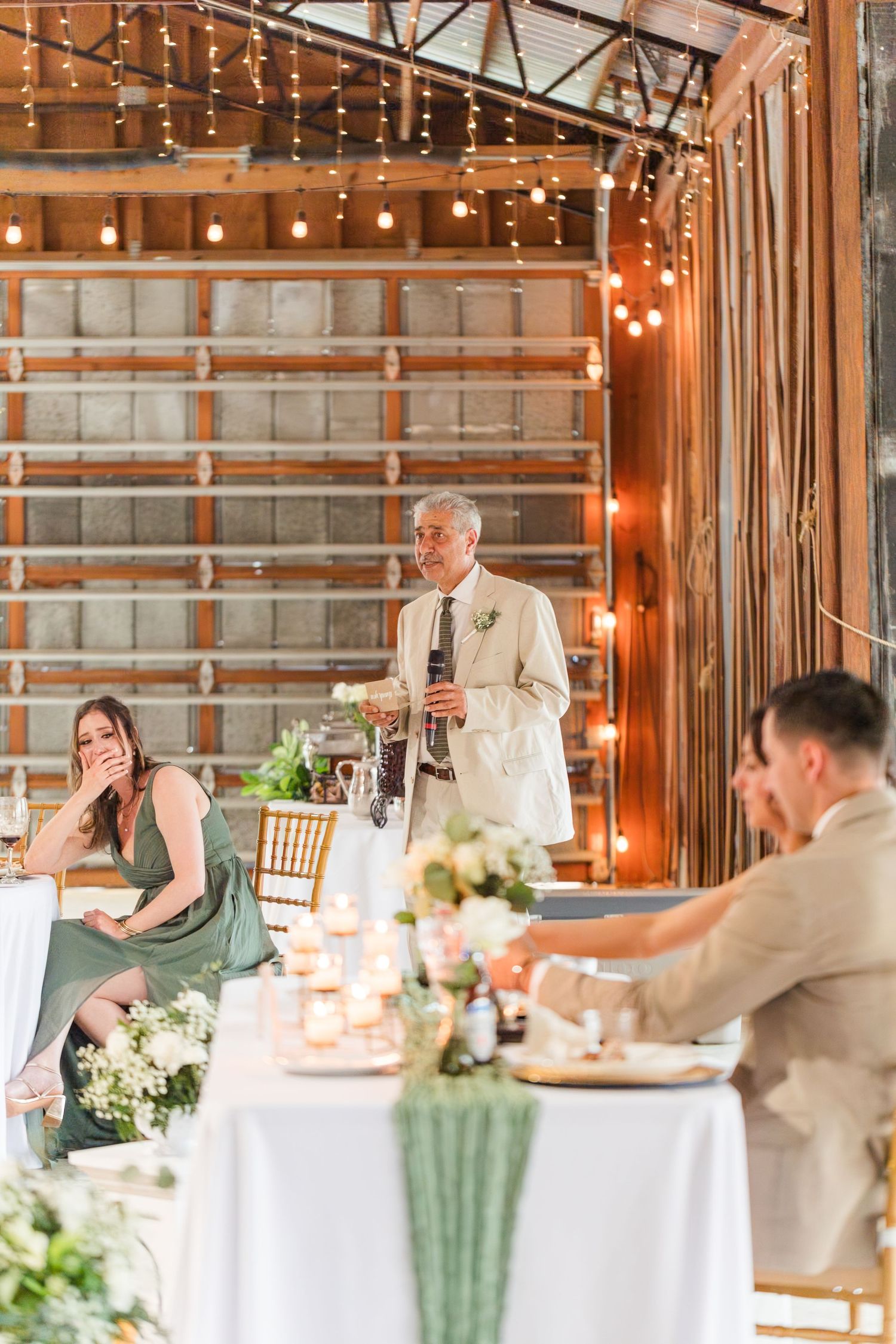 Wedding reception in a rustic barn venue decorated with string lights and white linens for an elegant dinner celebration.