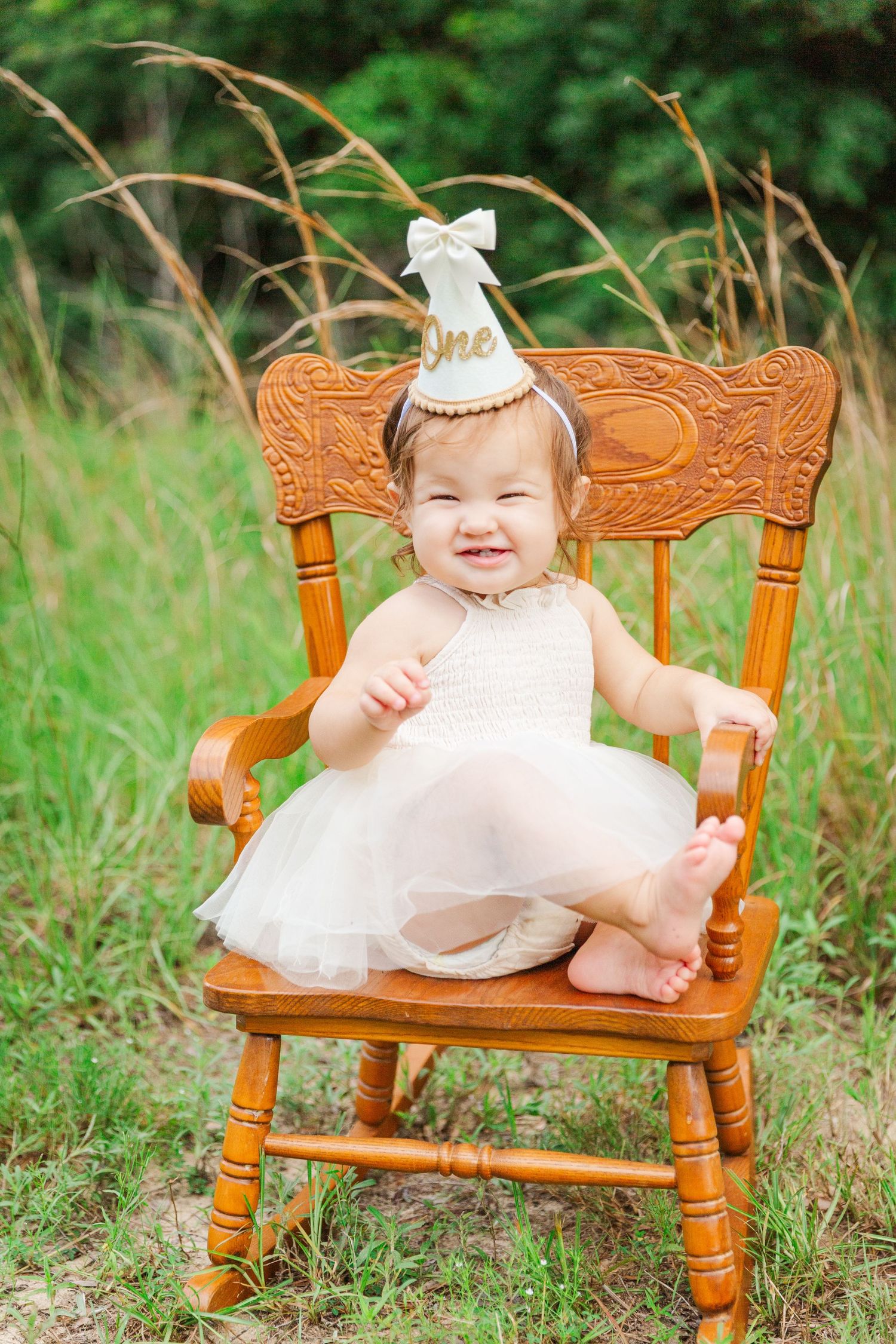 Small wooden rocking chair sits in tall grass with natural outdoor backdrop.