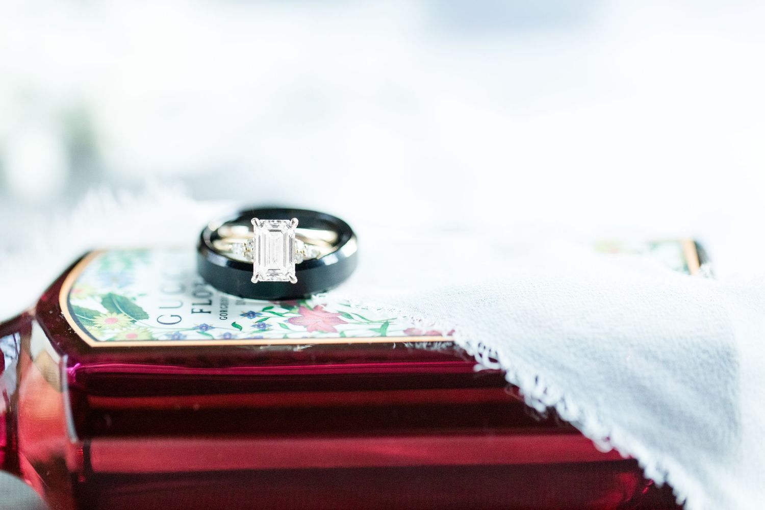 A wedding ring sits atop a red surface with a soft white background creating an elegant bridal detail shot.