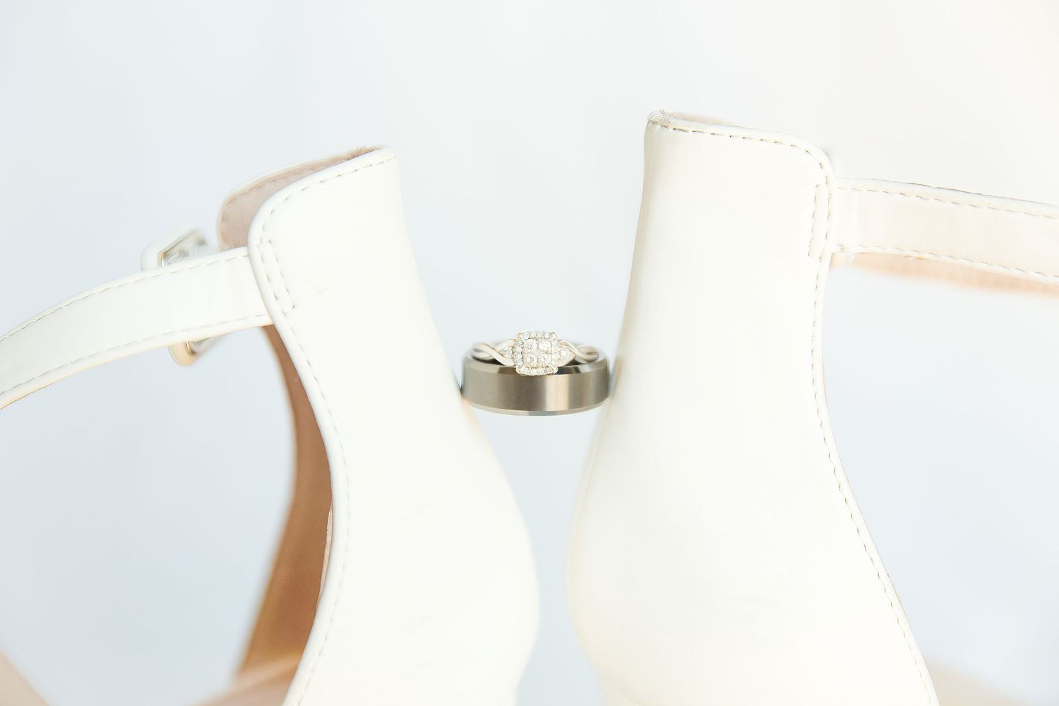 White wedding shoes and silver wedding rings arranged on light background.