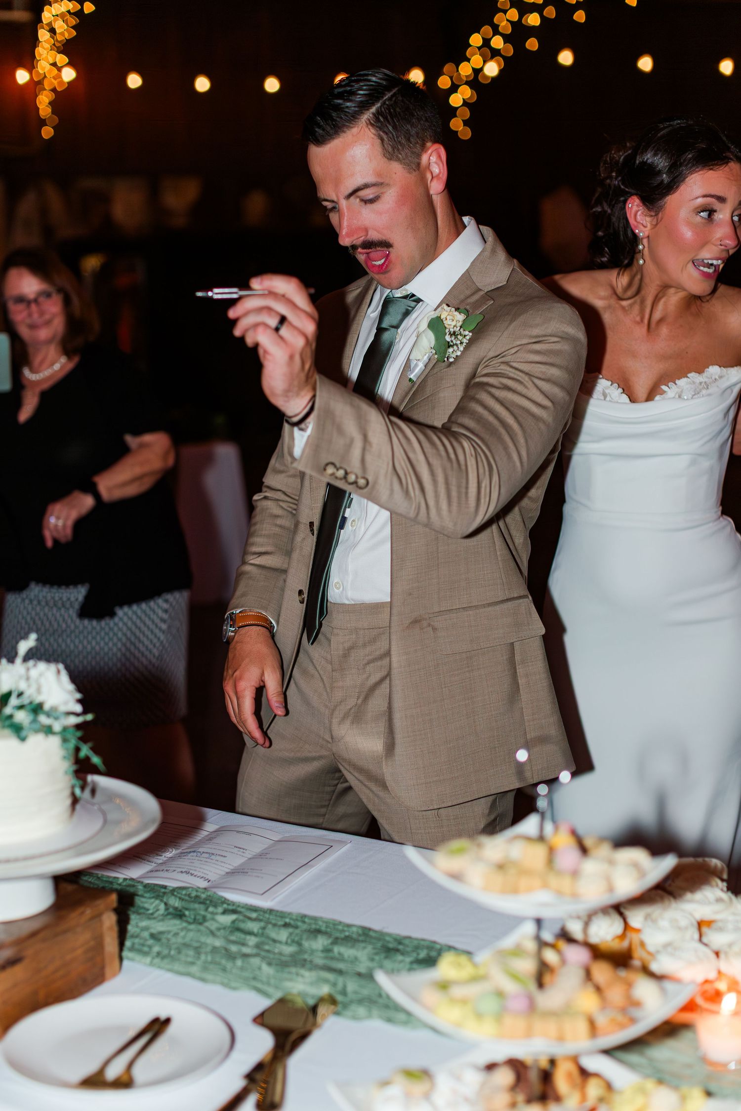 Wedding couple enjoying their cake cutting moment at a reception with twinkling lights in the background.