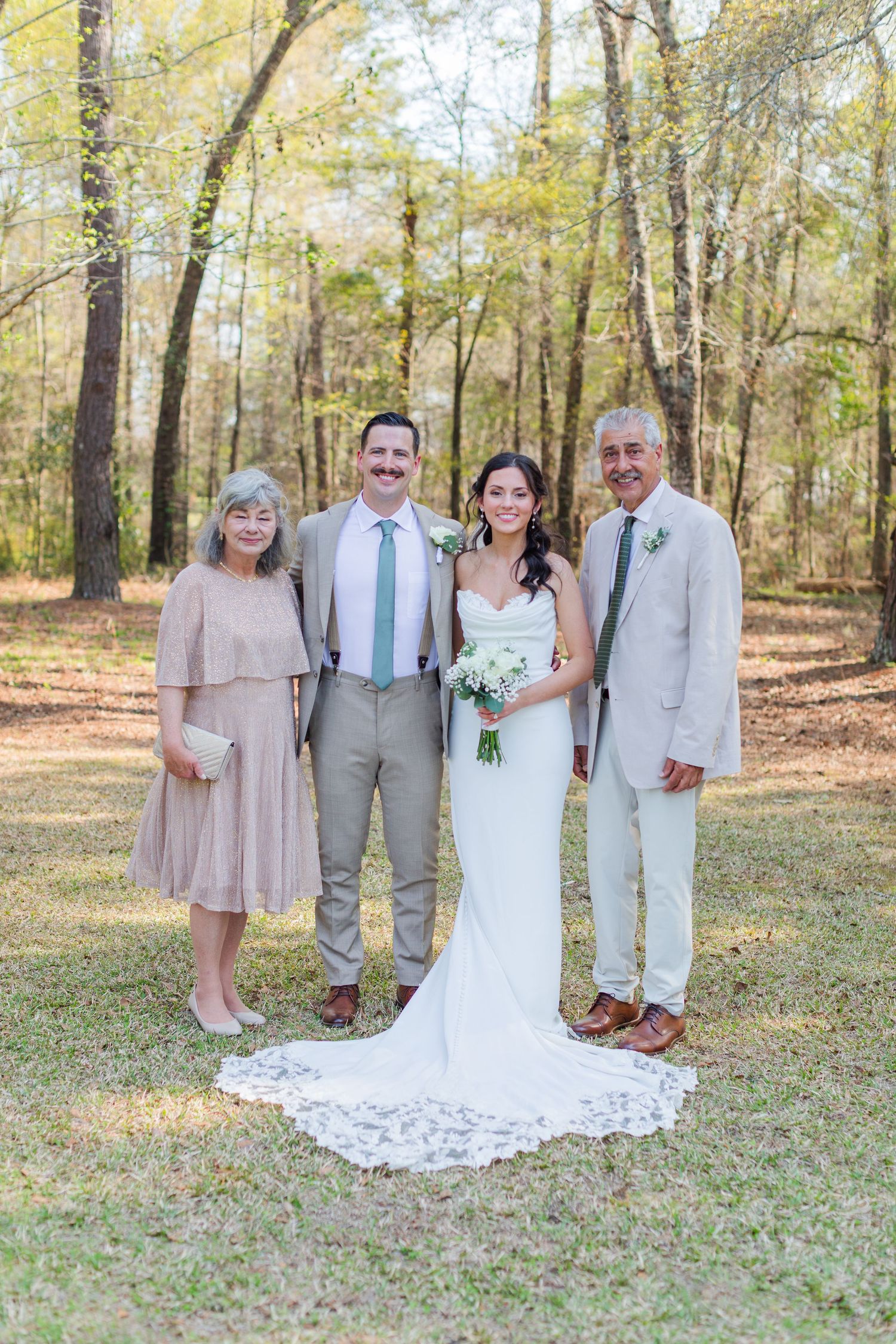 Wedding party in gray suits and blush dresses posing outdoors in a wooded autumn setting.