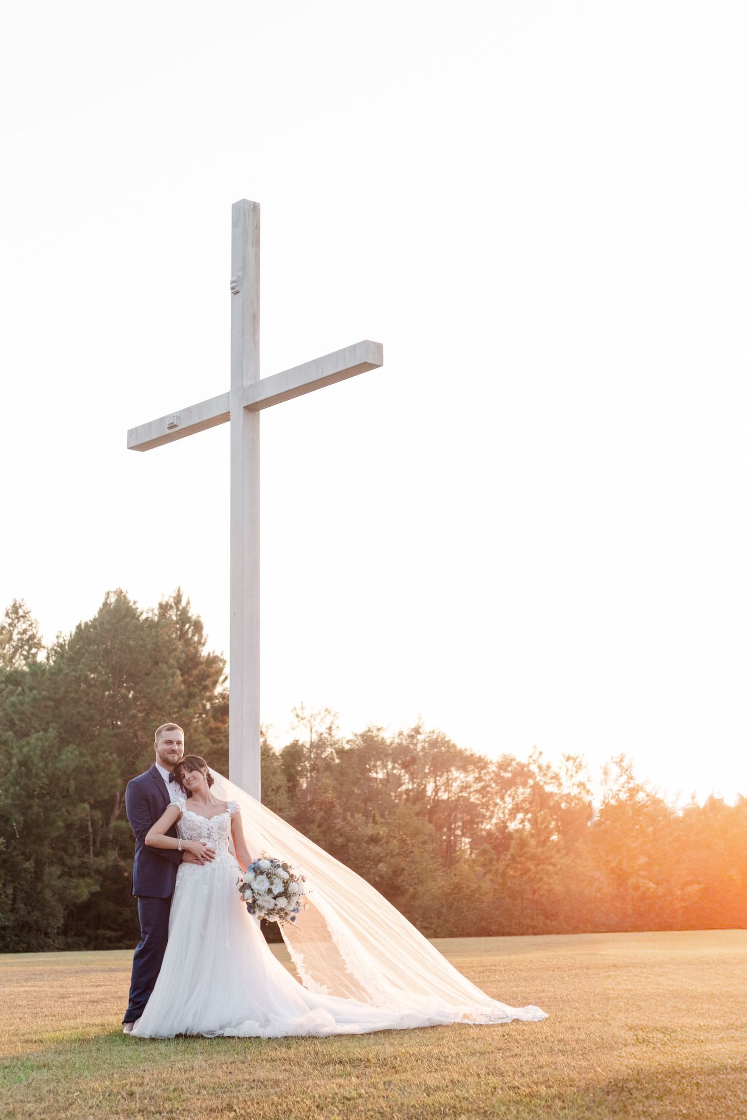 Romantic wedding portraits at sunset with crosses in an open field setting.