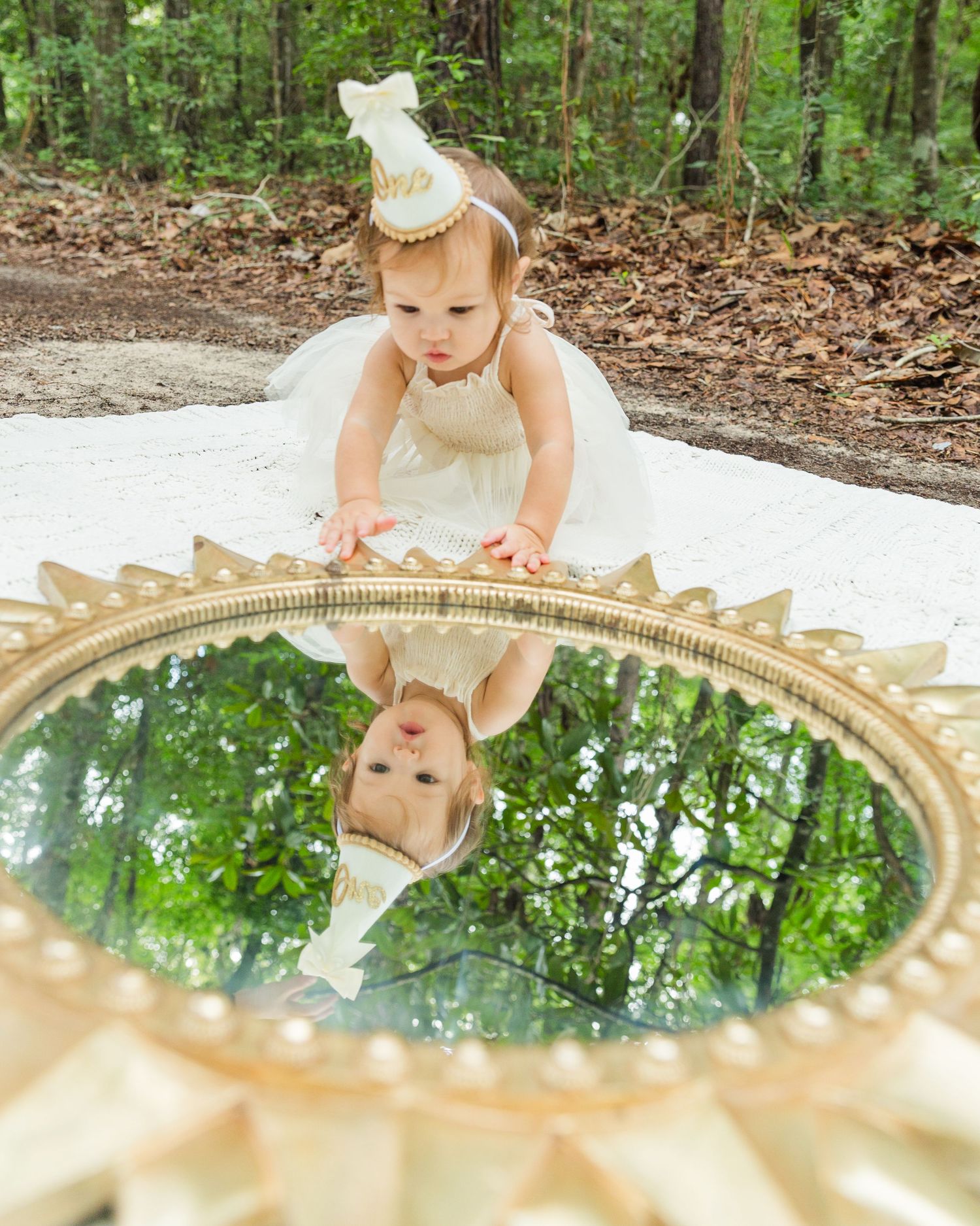 Decorative gold sunburst mirror reflects trees and sky in outdoor woodland setting.