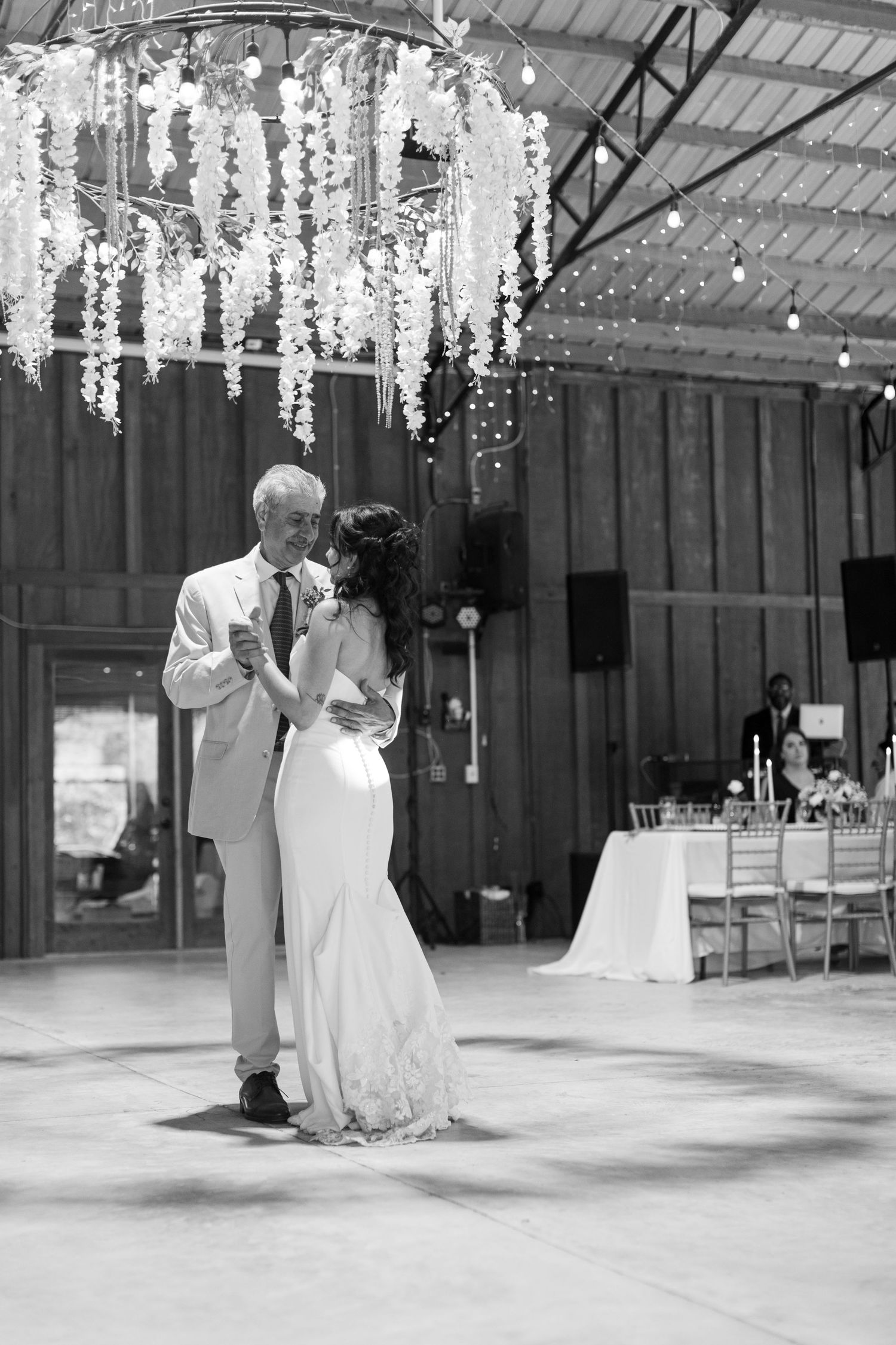 Couple shares their first dance under hanging floral arrangements in rustic barn wedding venue.