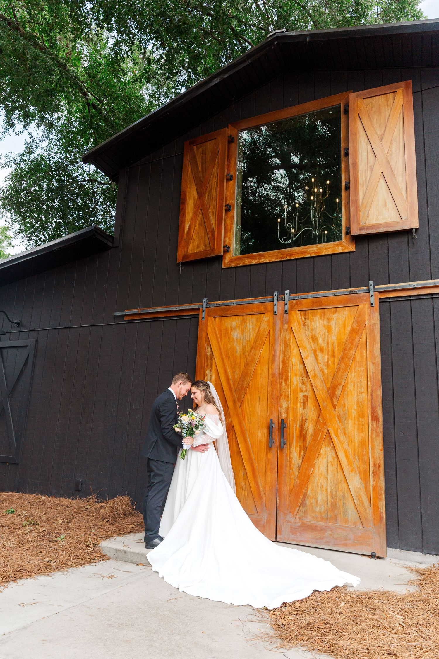 Wedding couple poses against black barn with wooden doors for rustic outdoor portraits.
