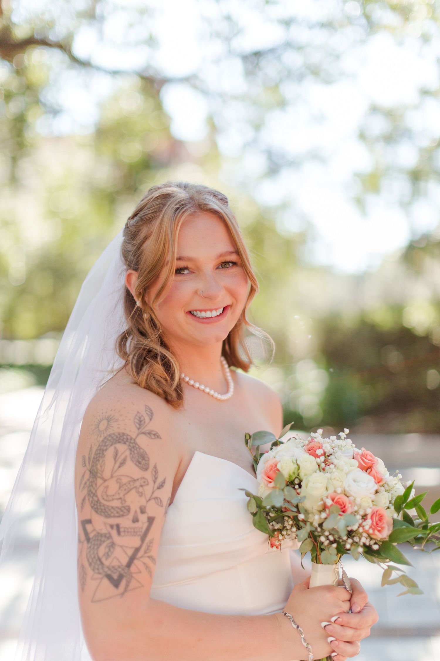 Bridal portrait outdoors holding coral and white floral bouquet.