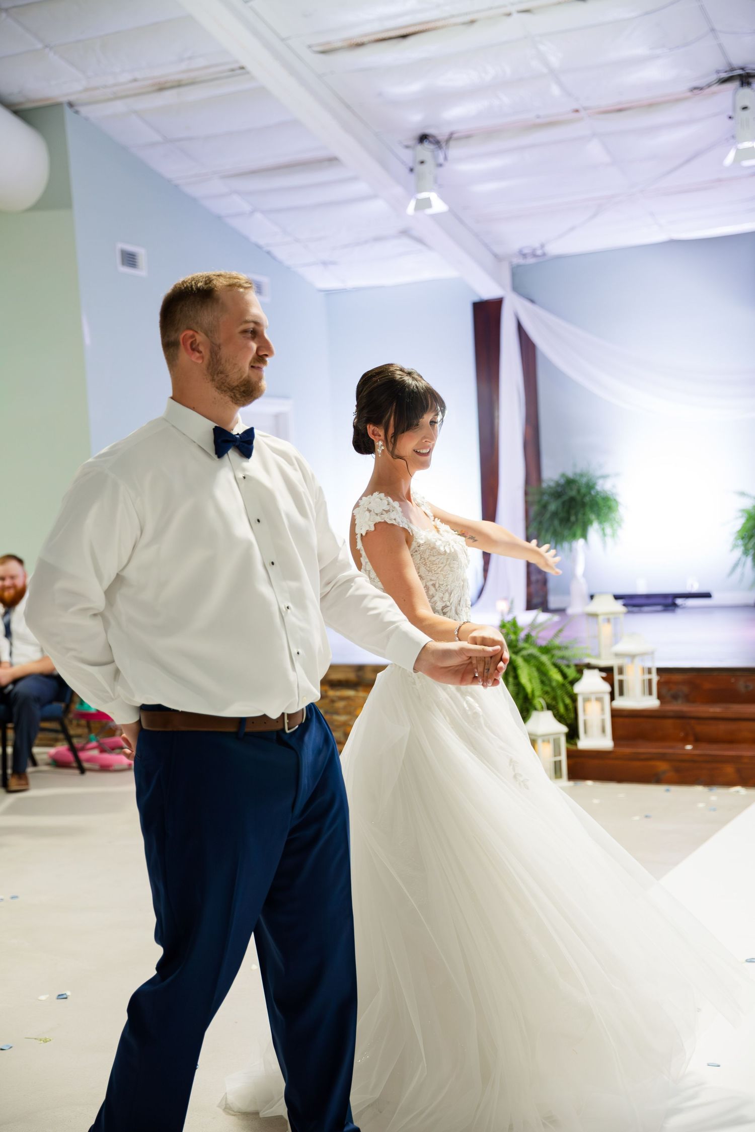 Couple dancing together on wooden floor, bride wearing flowing white gown.