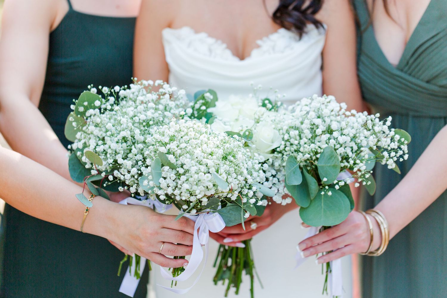 Wedding party members hold delicate white baby's breath bouquets with green eucalyptus accents against forest green dresses.