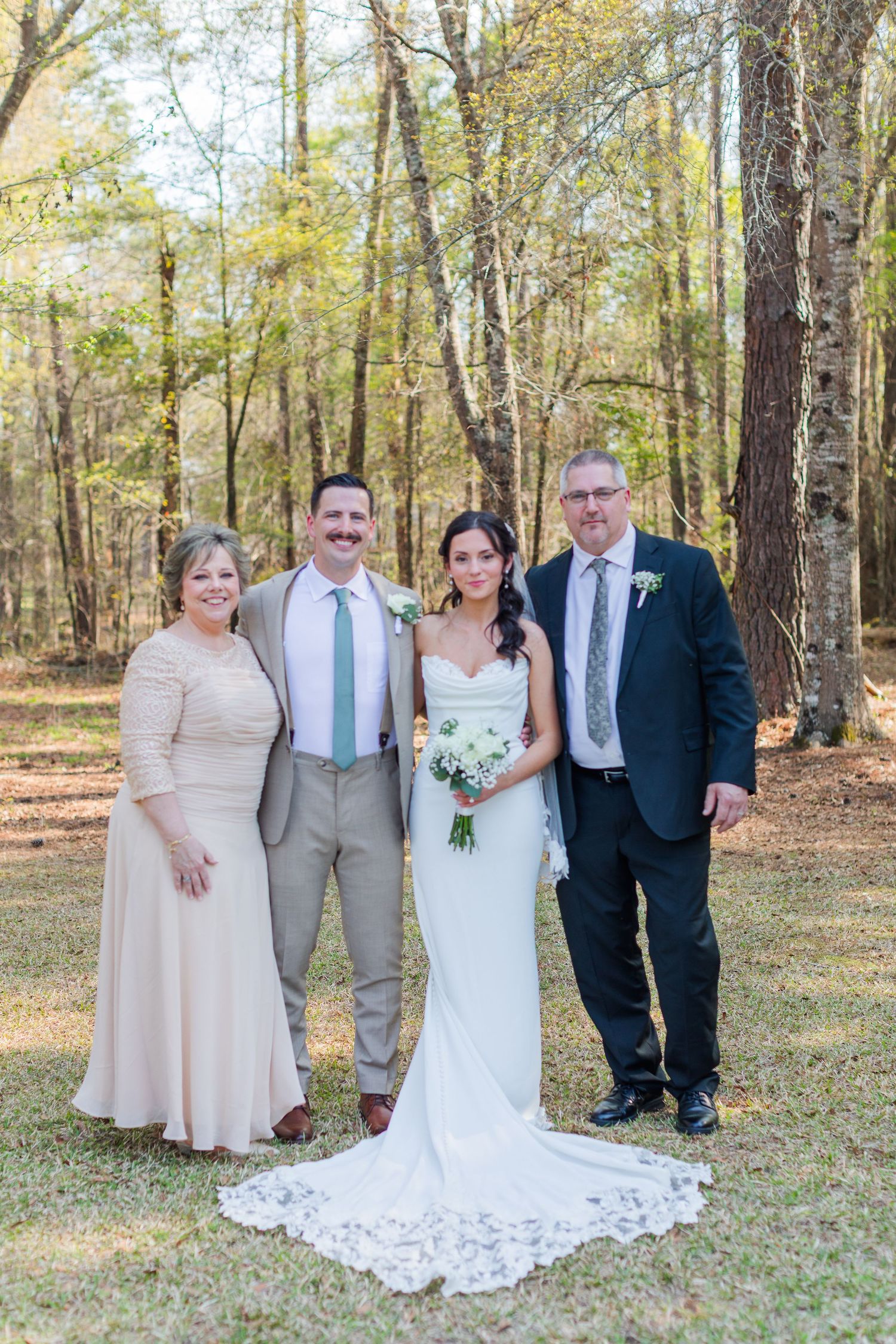 A wedding party poses together in a sunlit autumn forest setting with fallen leaves.
