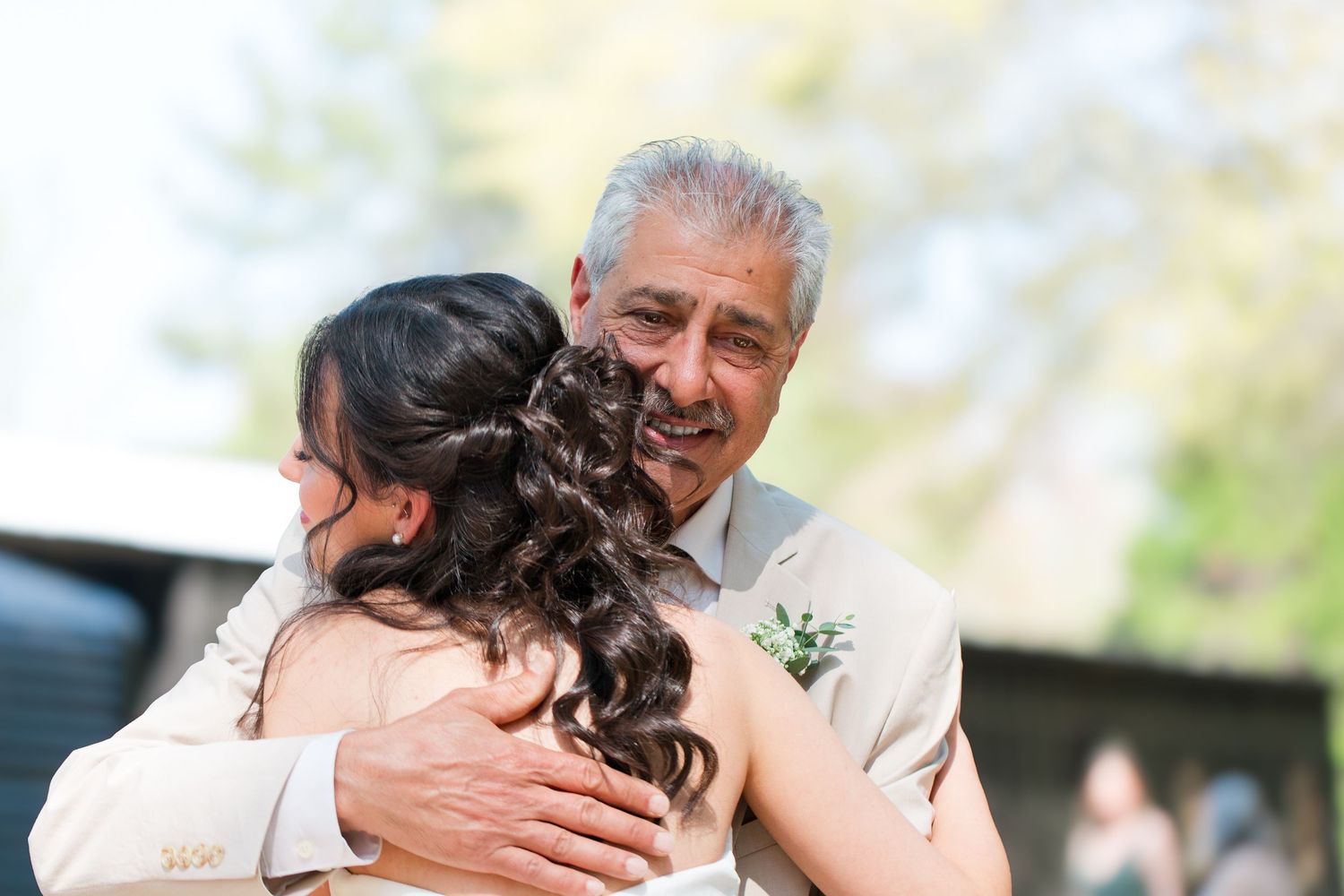 Two people embrace warmly at an outdoor gathering with joyful expressions and natural lighting.