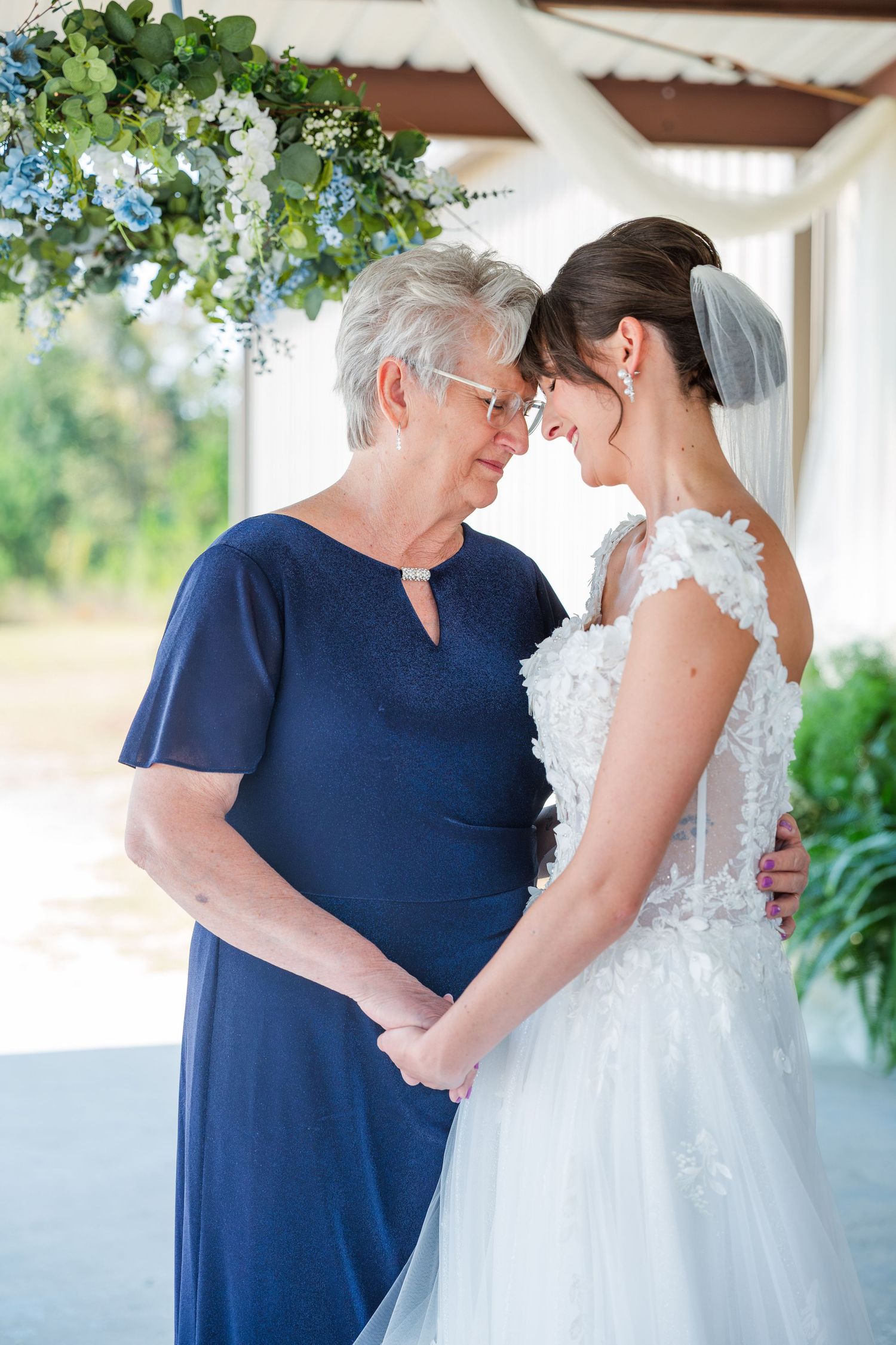 An emotional moment between a bride in a white gown and her mom in navy blue during a wedding celebration.