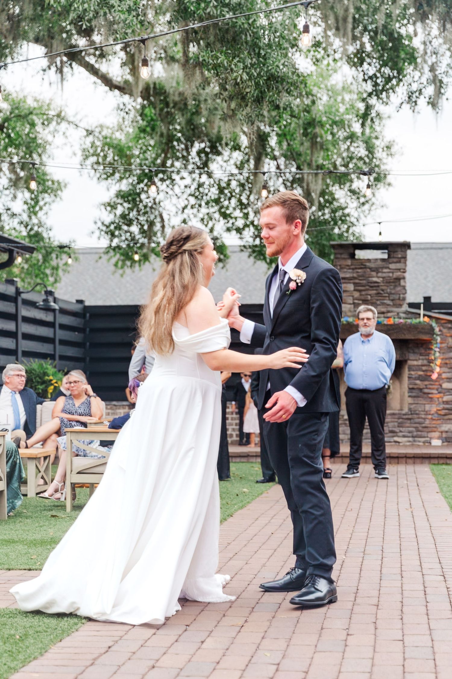 Couple dancing on brick patio under hanging tree branches.