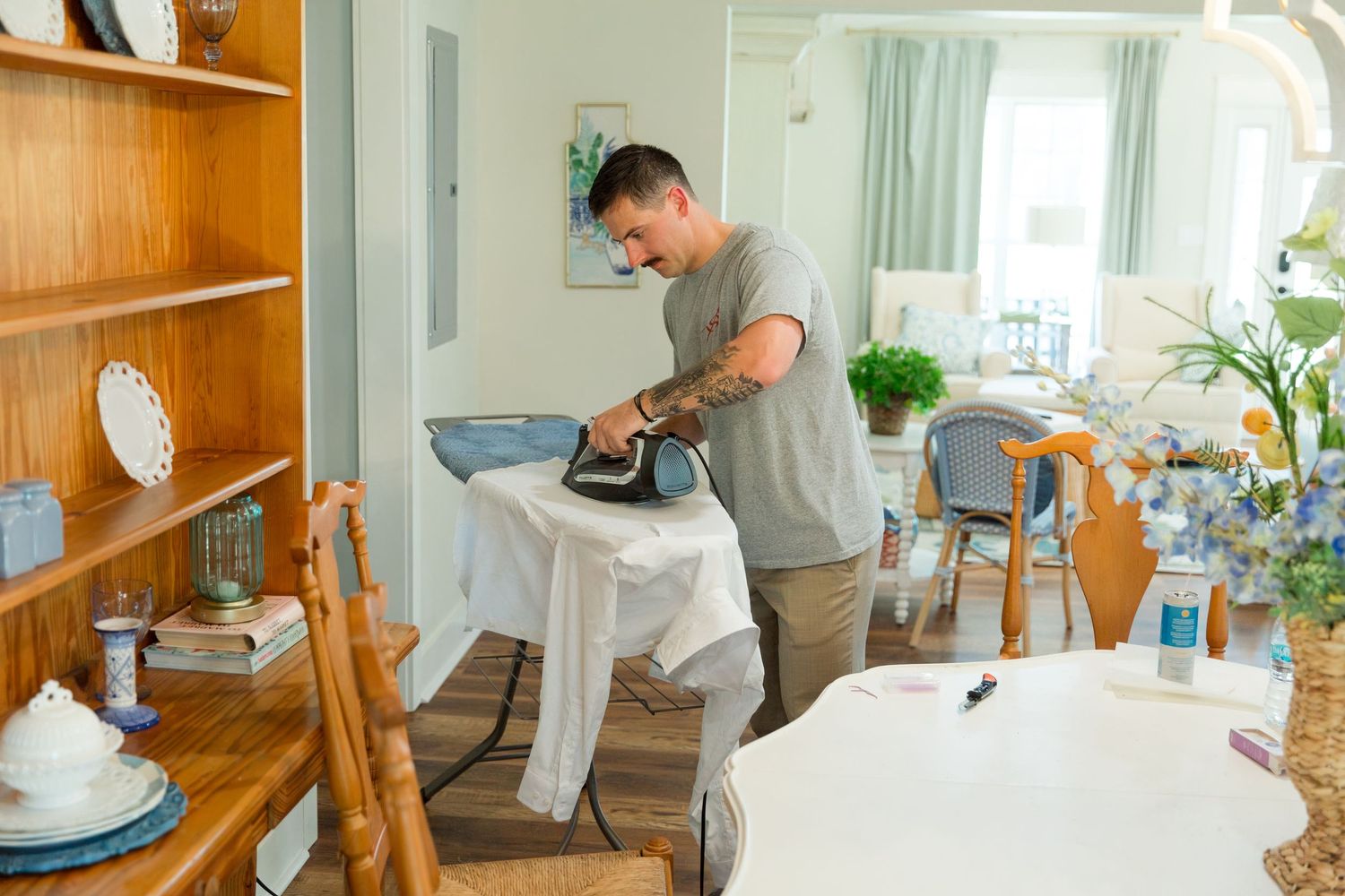 A person installing a wooden shelf on a wall using power tools and mounting brackets in a bright room.