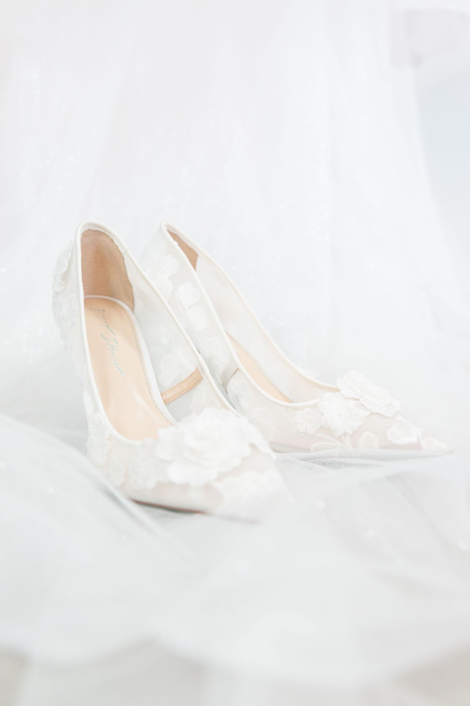 Elegant white lace bridal shoes photographed on light background.