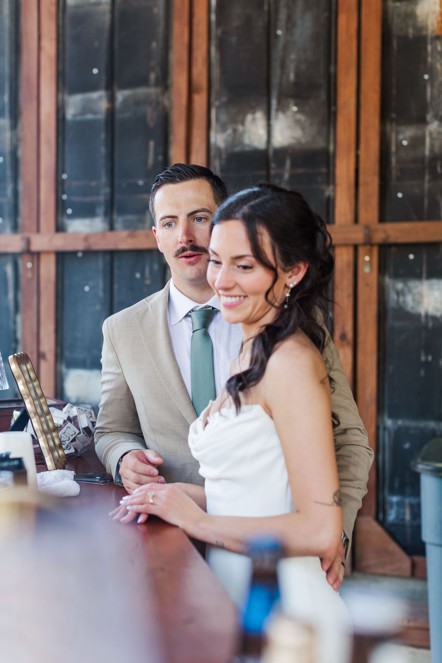 A couple shares an intimate moment while sitting at a rustic wooden table during their wedding reception.