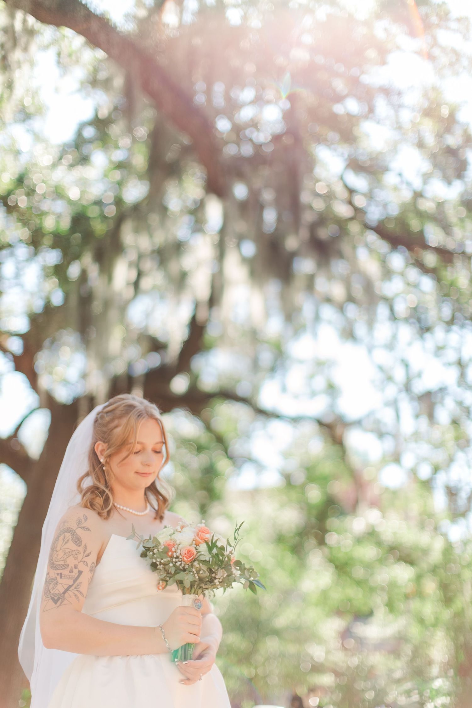 Bride poses with bouquet in sunlit garden setting with Spanish moss in background.