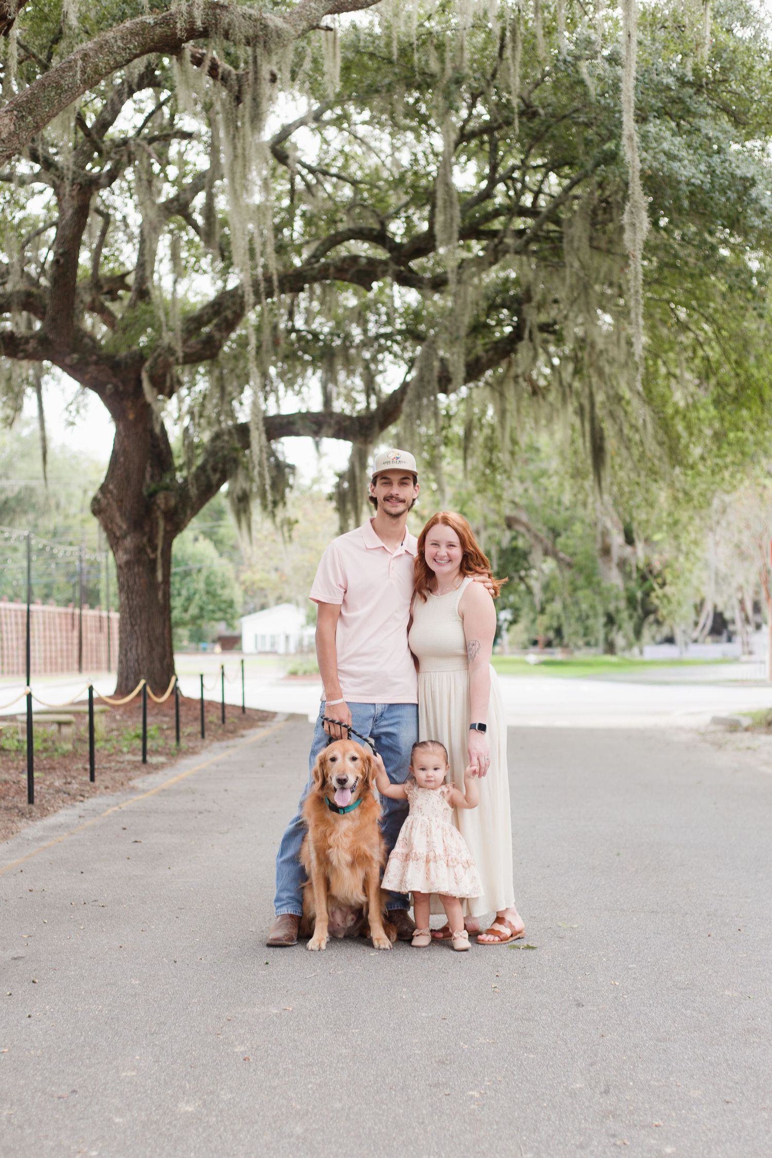 Family photo session on tree-lined path with dog.