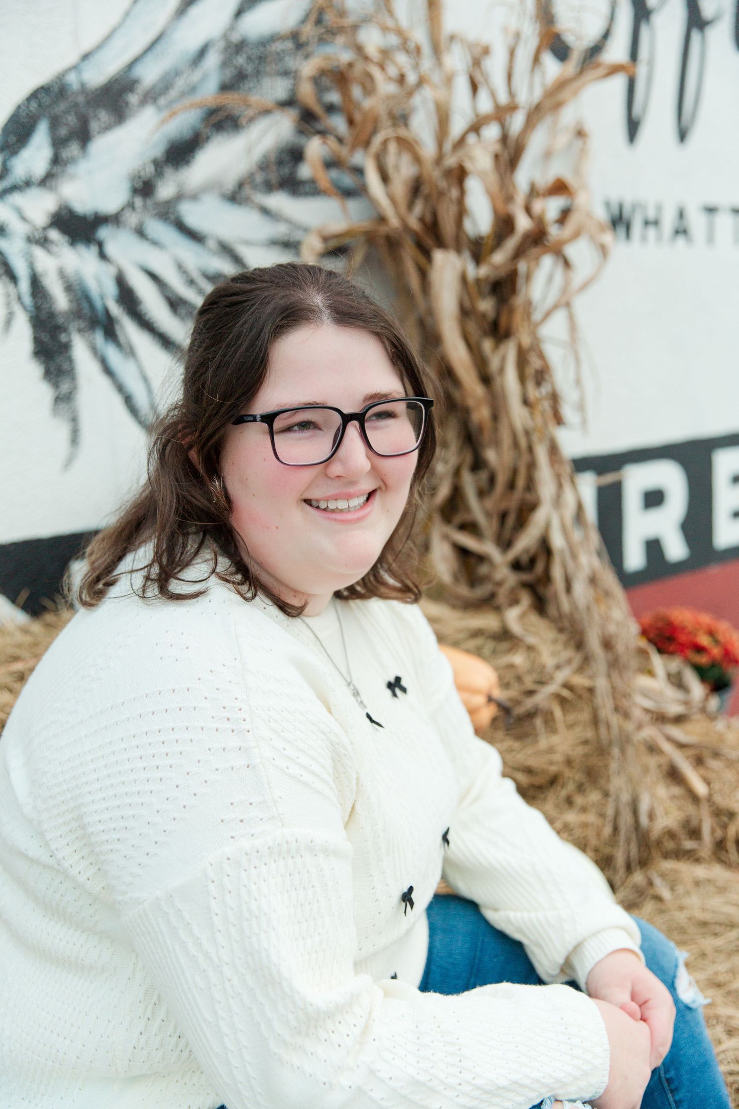 Person in white sweater poses against rustic backdrop with natural decor.