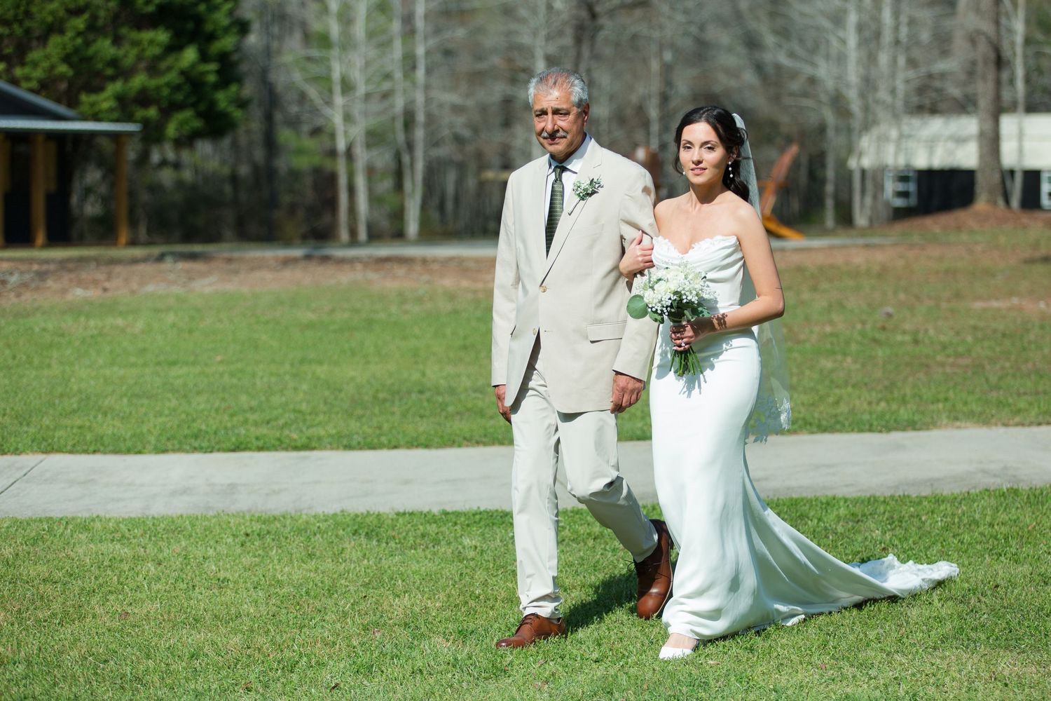 A couple walking together outdoors on their wedding day in elegant light-colored formal attire.