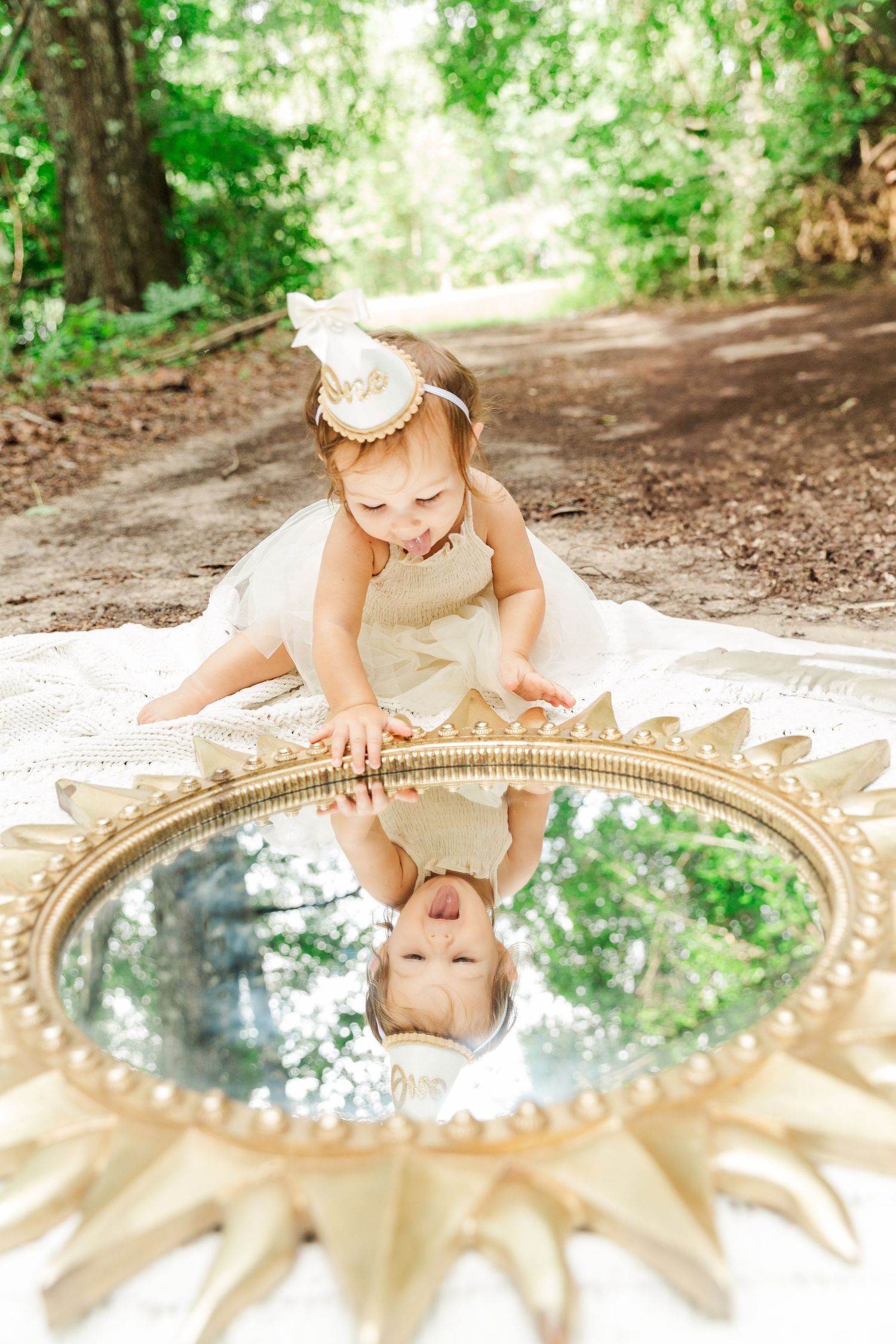 Ornate gold mirror placed on ground reflects green forest canopy above.