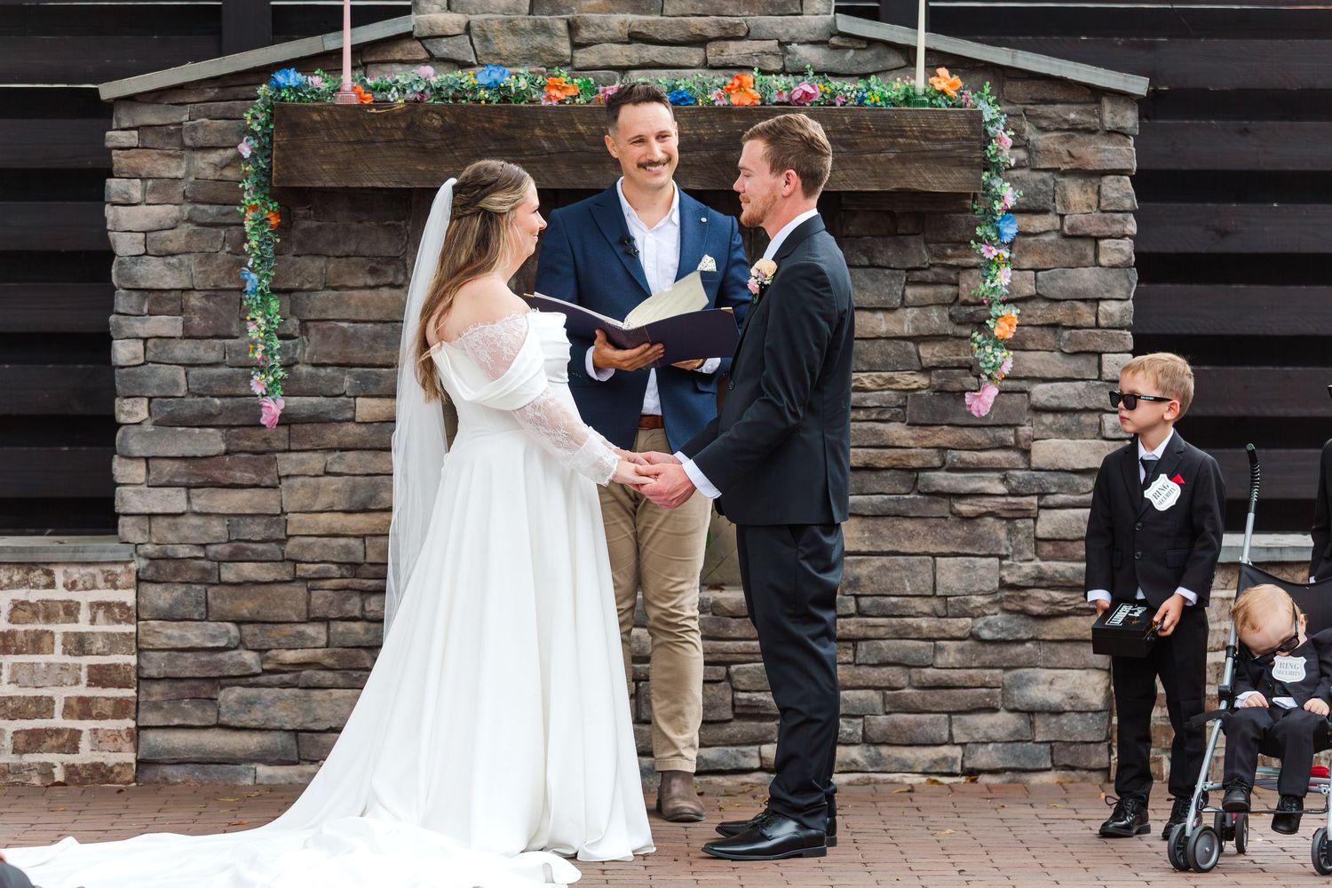 Wedding ceremony taking place in front of stone archway with floral decorations.
