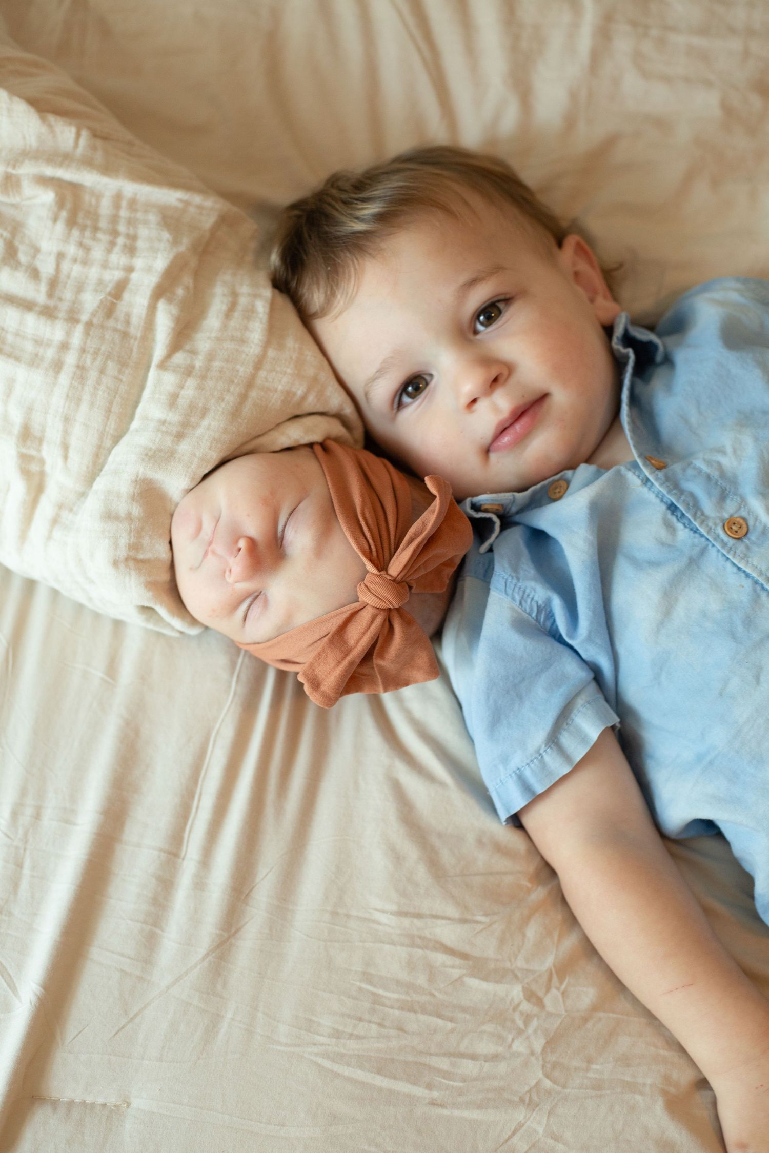 A child rests peacefully on cream-colored bedding wearing blue and brown clothing.