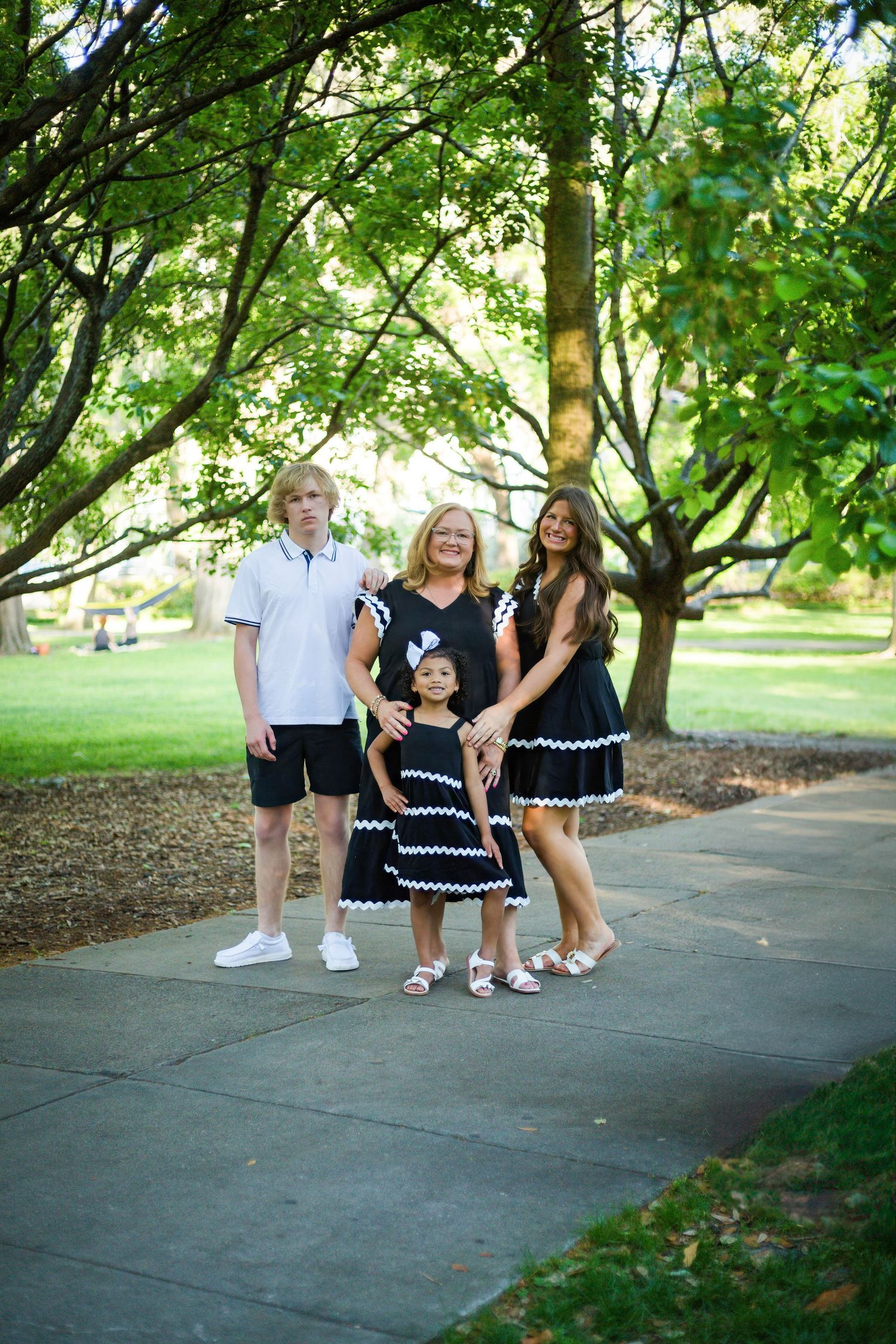 A group in coordinated black and white outfits poses playfully on a tree-lined path.