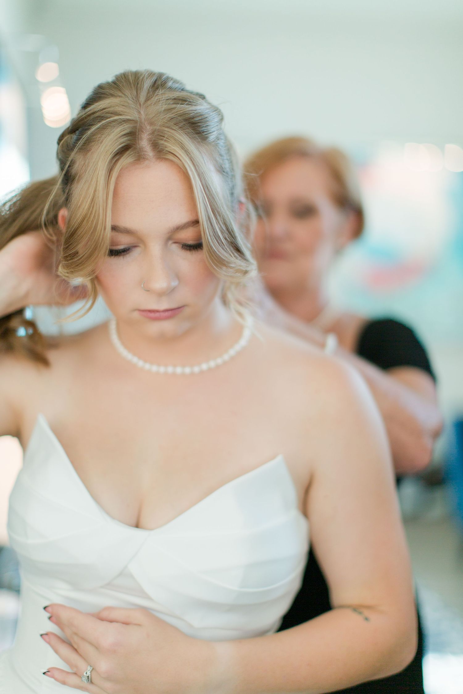 Bride in white dress with pearl necklace looking down during wedding preparations.